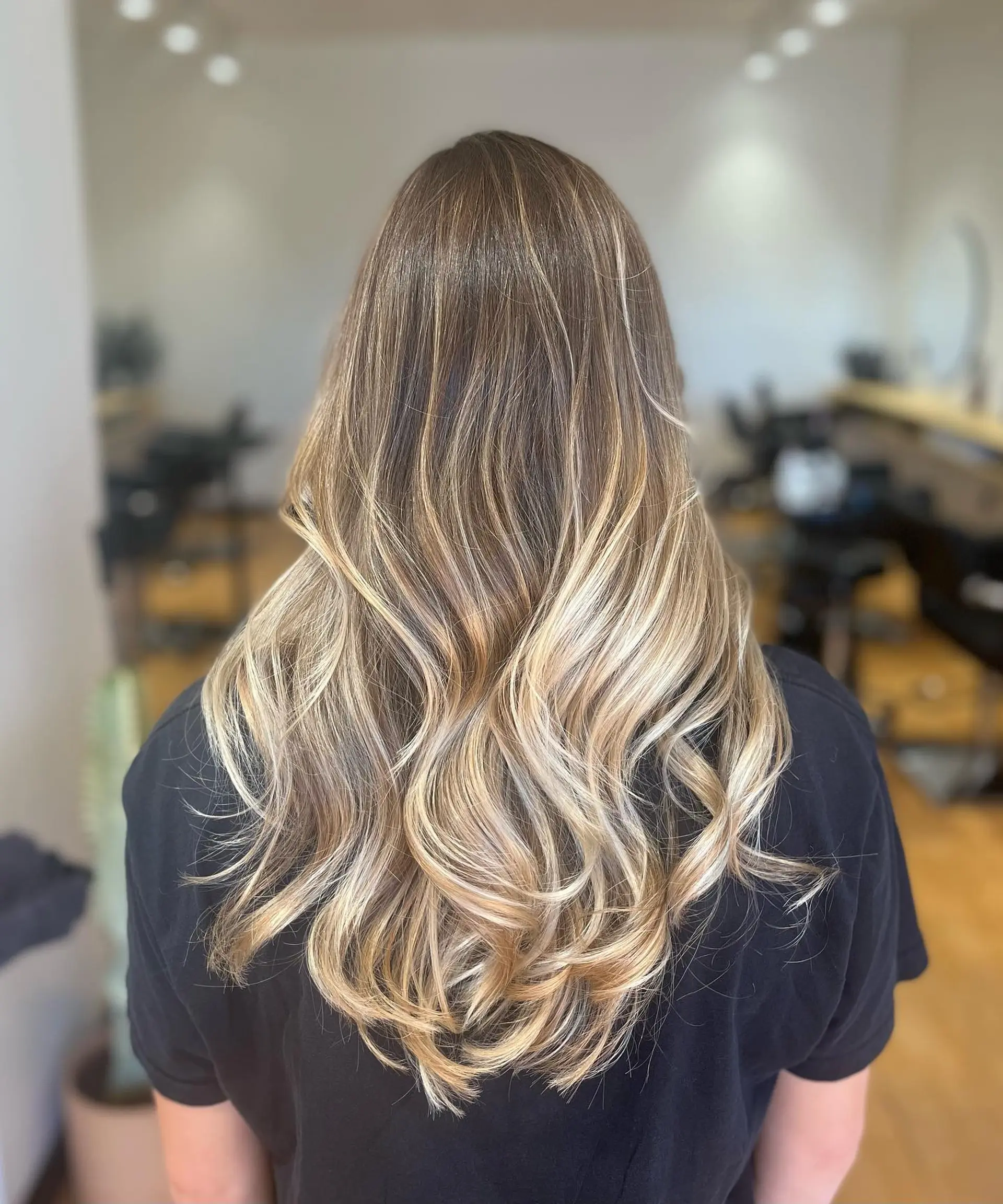 Long hair featuring a seamless blonde balayage over a natural light brown base, styled in loose, flowing waves. 1