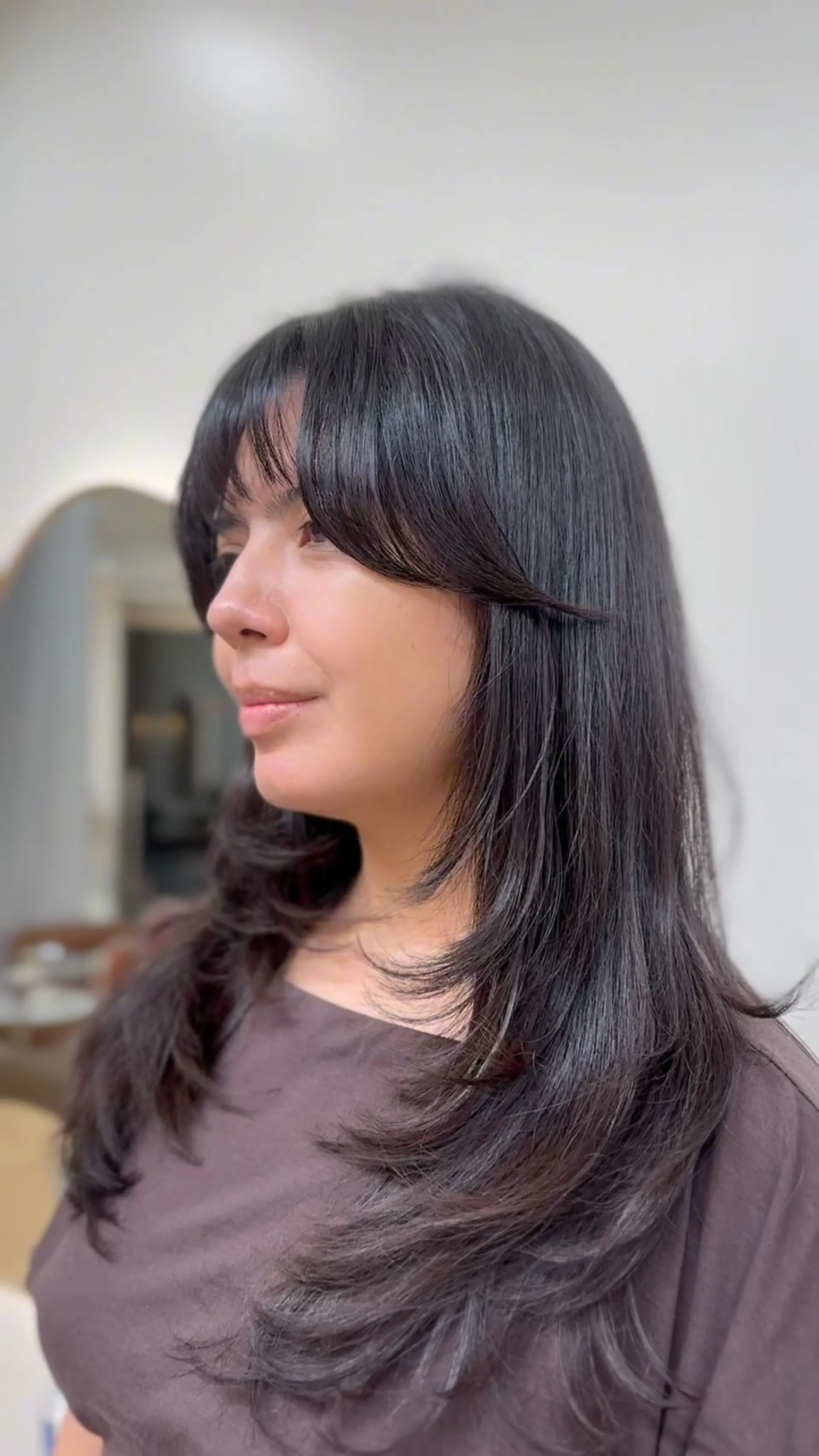 Long dark hair styled with high feathered layers, soft face-framing strands, and airy curtain bangs. 1