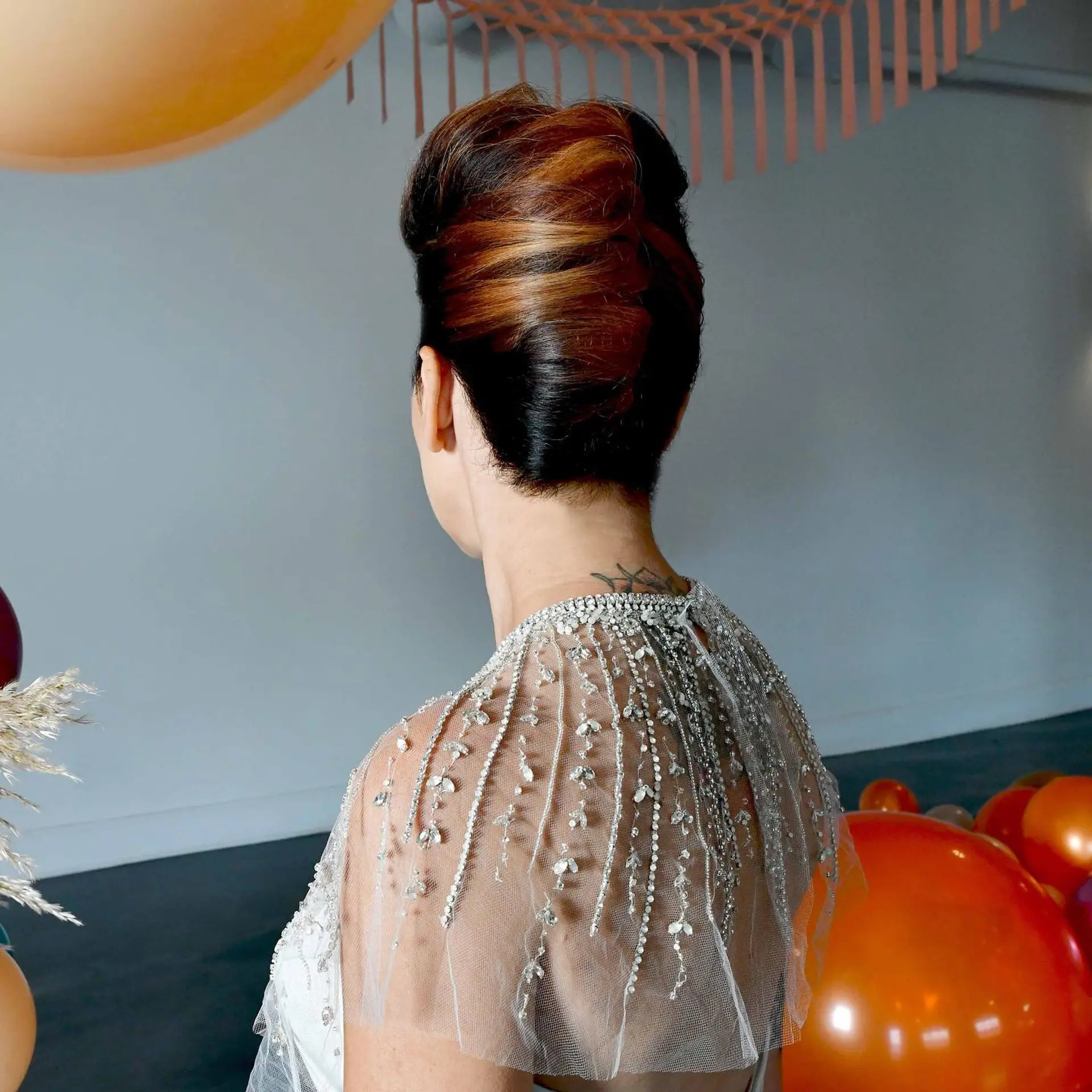 A sleek, sculpted vertical French twist updo highlighting warm copper tones against dark hair. 1