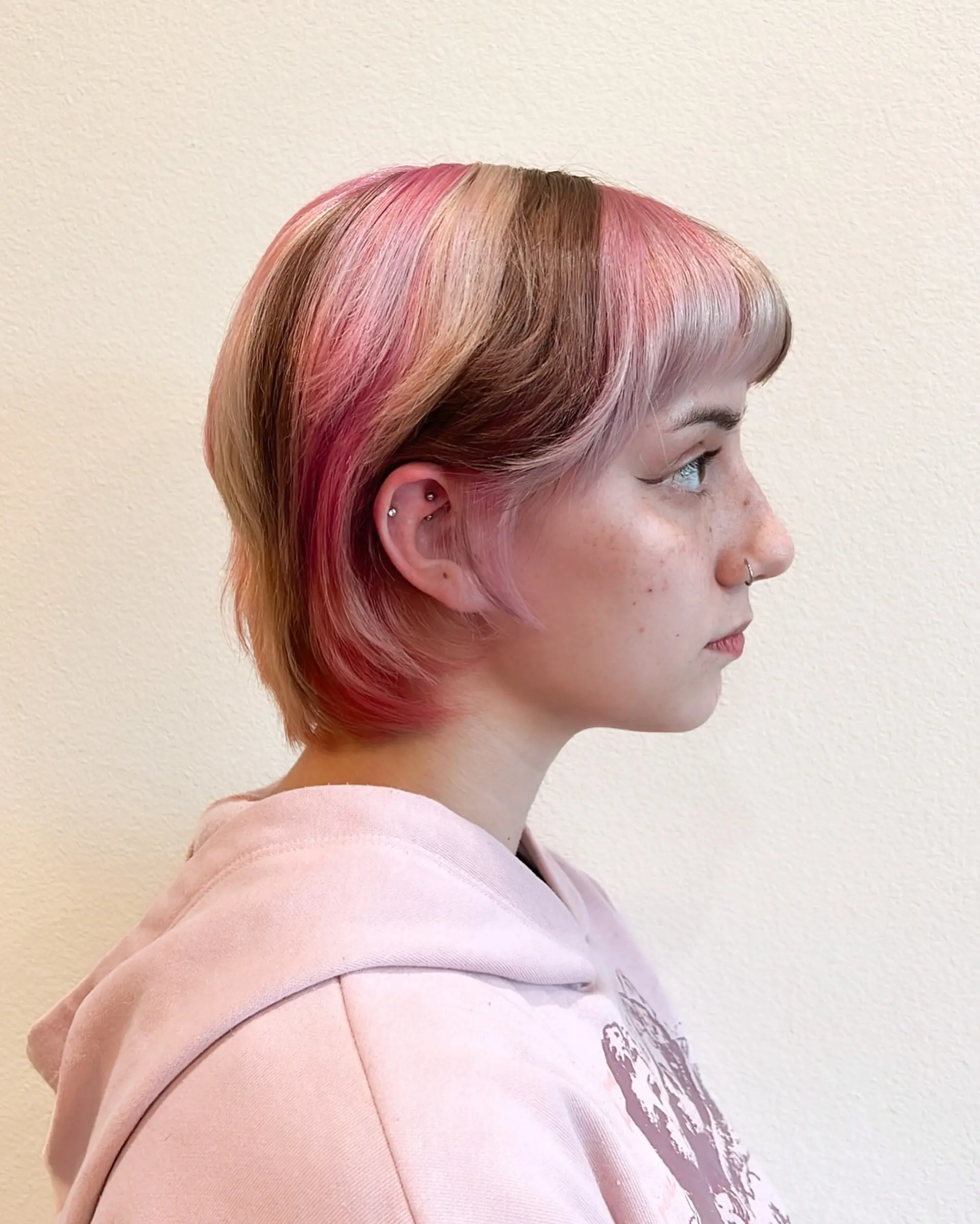 This bold pixie bob features a multi-tonal color block design, incorporating vivid and pastel pinks, light blonde, and a dark brown section for a striking contrast. The cut is layered, ending above the nape, and styled with a blunt fringe. 1