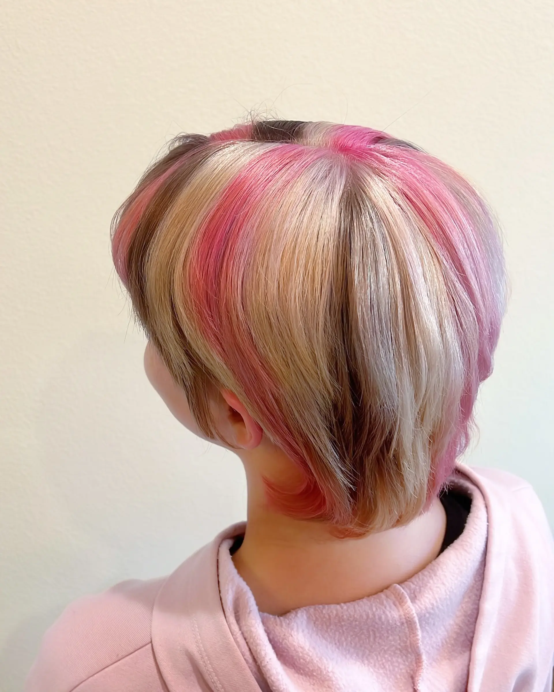 This bold pixie bob features a multi-tonal color block design, incorporating vivid and pastel pinks, light blonde, and a dark brown section for a striking contrast. The cut is layered, ending above the nape, and styled with a blunt fringe. 3