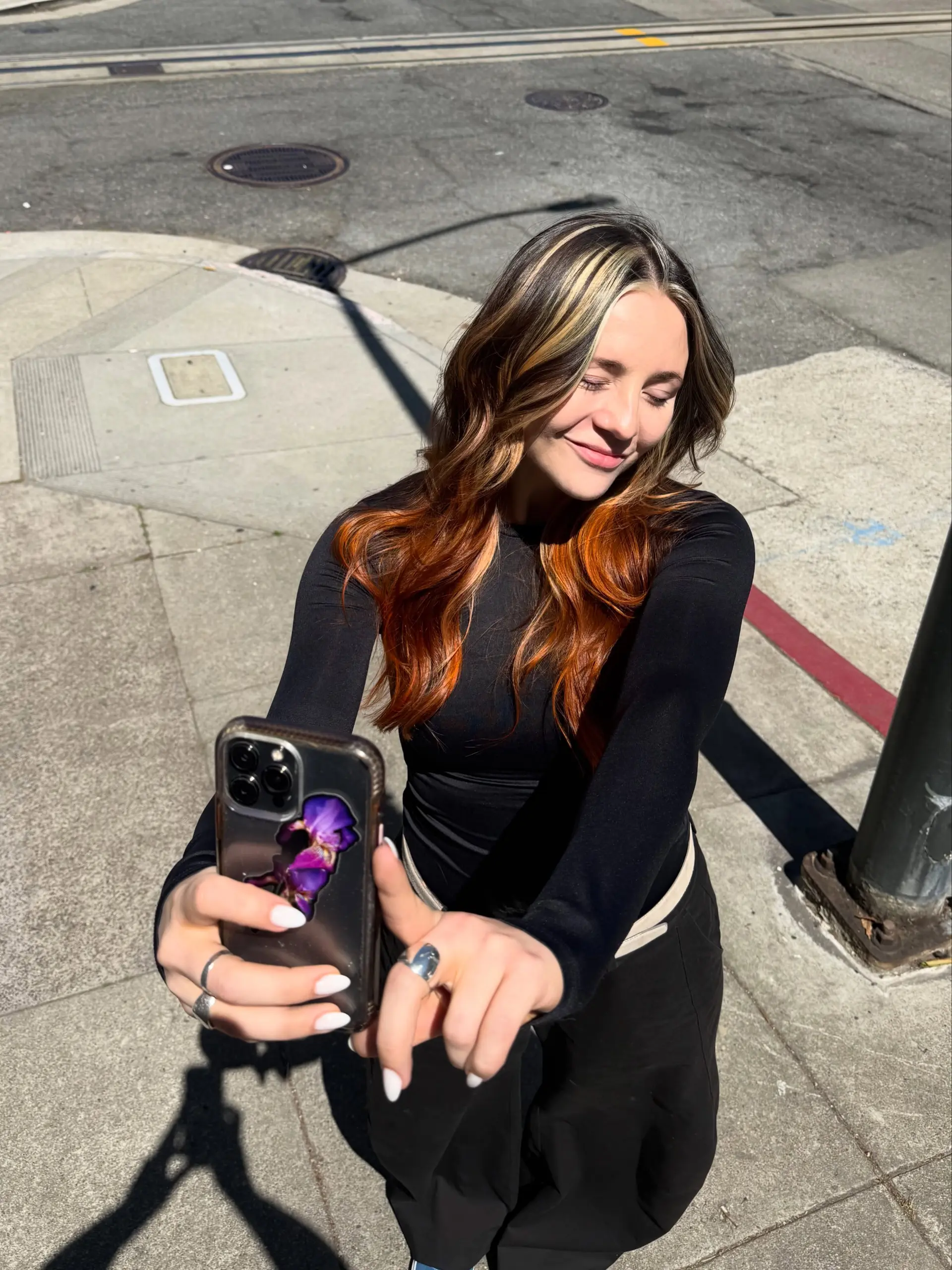 Long wavy brunette hair styled with chunky blonde face-framing highlights transitioning into rich copper ombré ends. 1