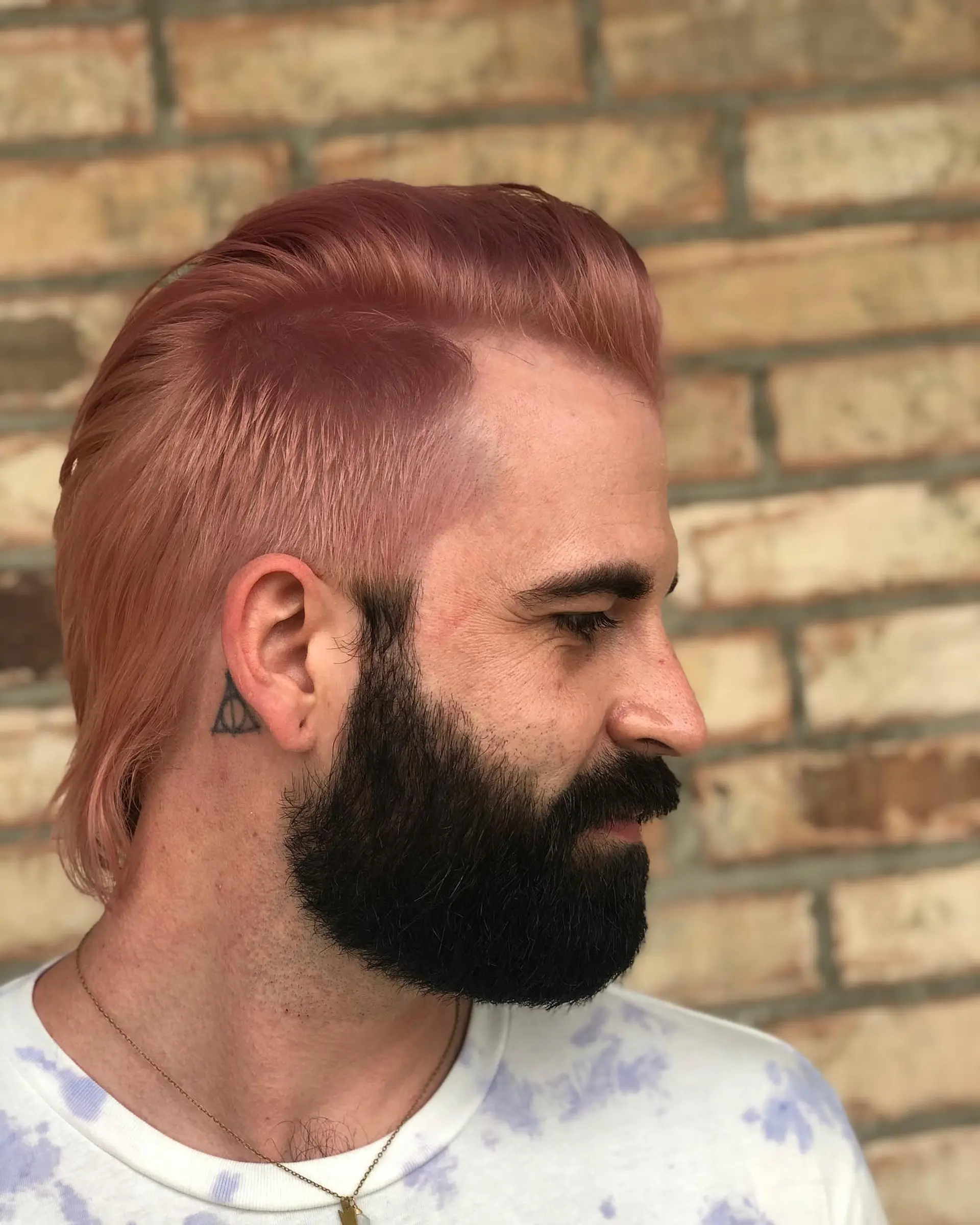A modern mullet colored in a soft pastel pink sorbet tone with cropped sides and styled volume on top. 1