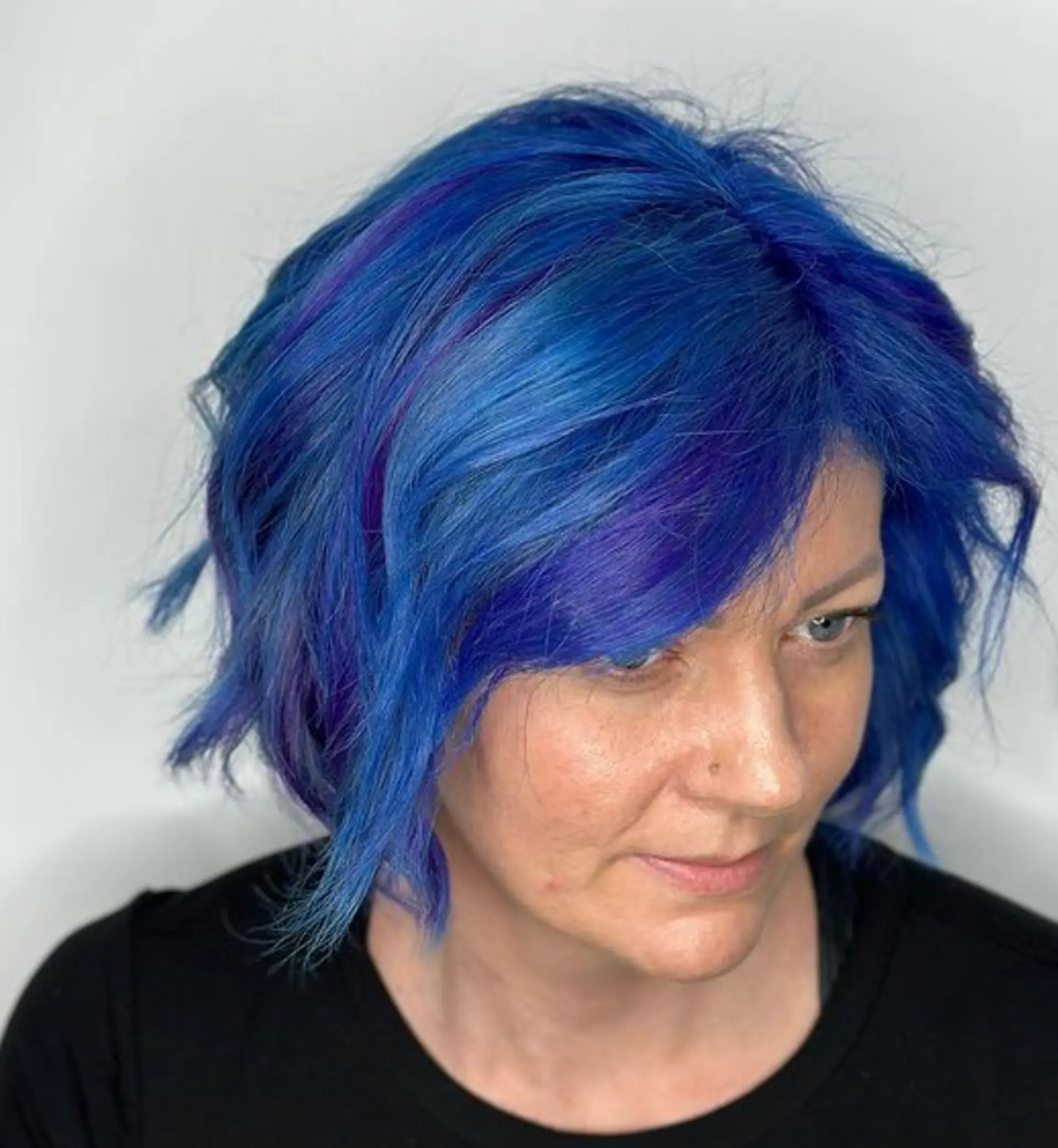 A short, wavy bob with vivid blue and indigo tones, featuring textured layers, a side-swept fringe, and tousled waves for a lively, youthful appearance.

Color by @simabeautynyc
Cut and style by @juliamannino_hair
 1