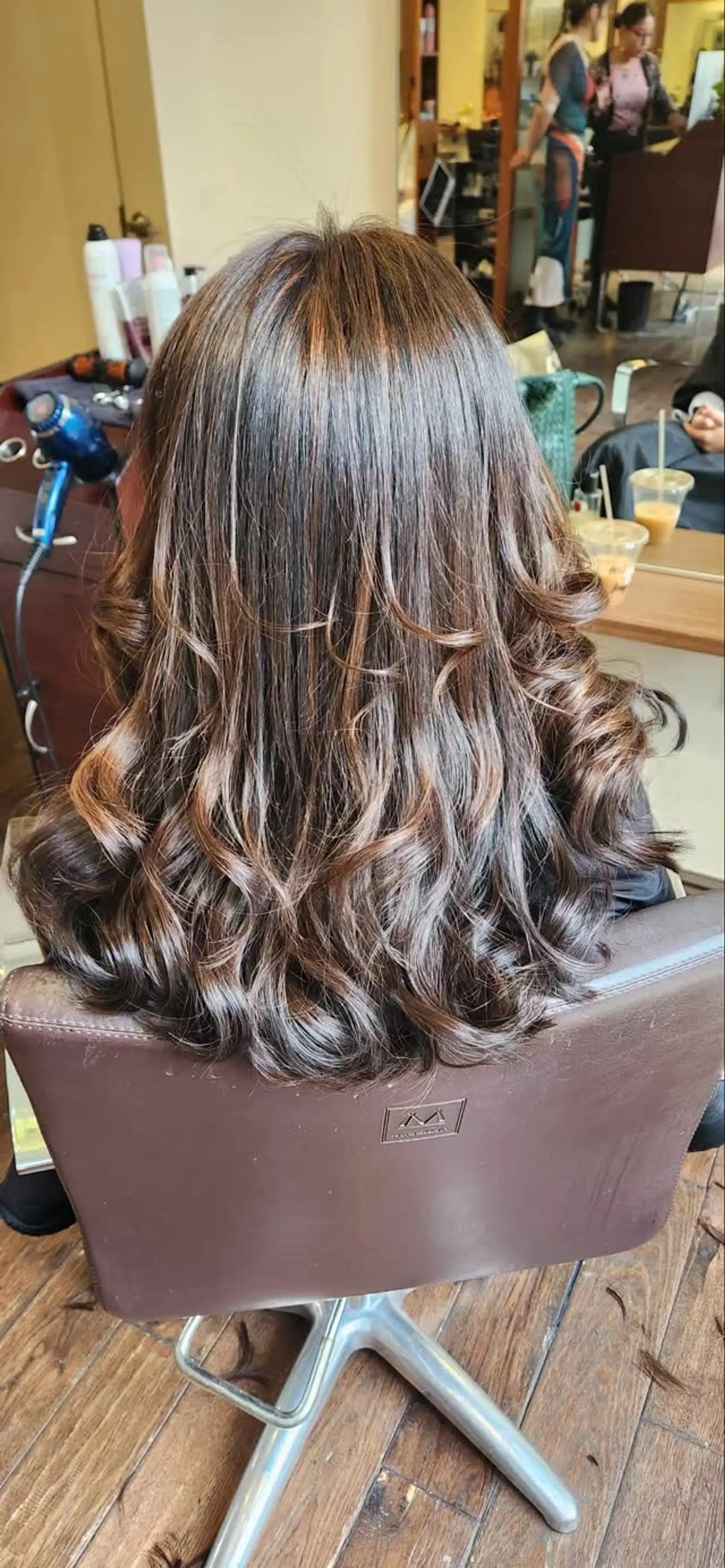 Long layered brunette hair with subtle warm caramel highlights styled into voluminous waves and curled ends. 1