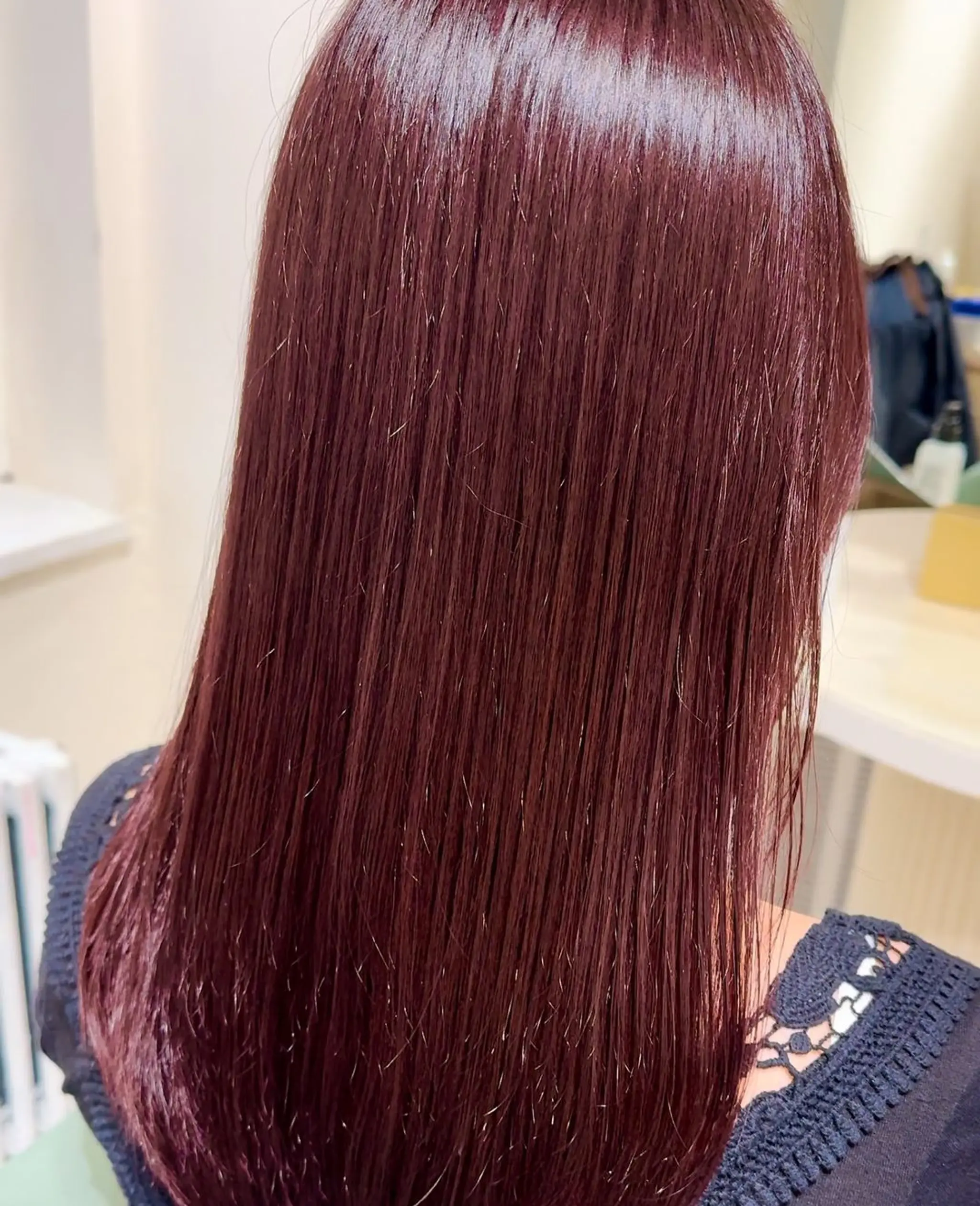 A sleek, shiny, and straight medium-length hairstyle with burgundy or crimson color, showcasing a glossy and chic appearance.