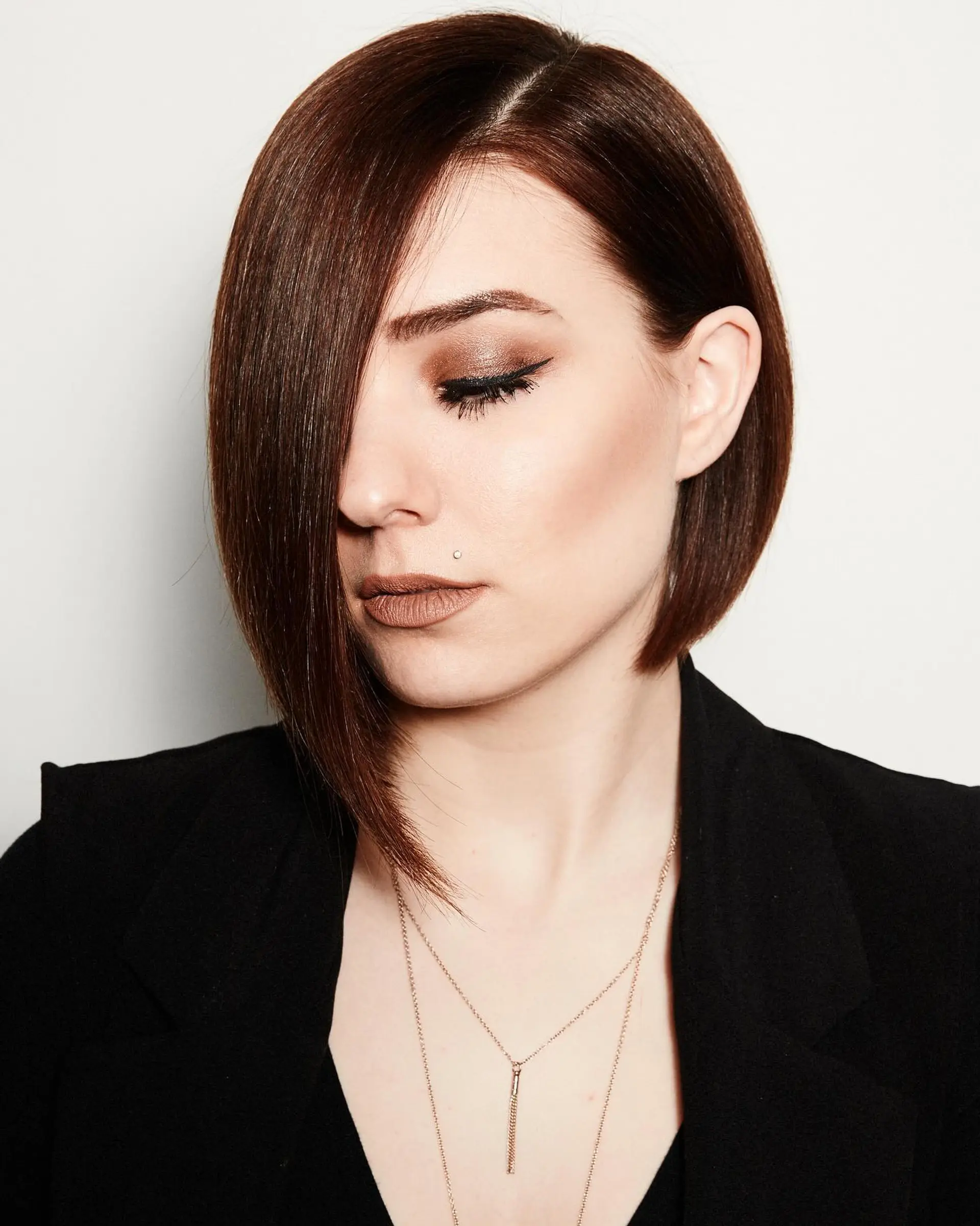 A sleek, precision-cut asymmetrical bob featuring a deep side part and a sharp, elongated front section in rich mahogany brown. 1