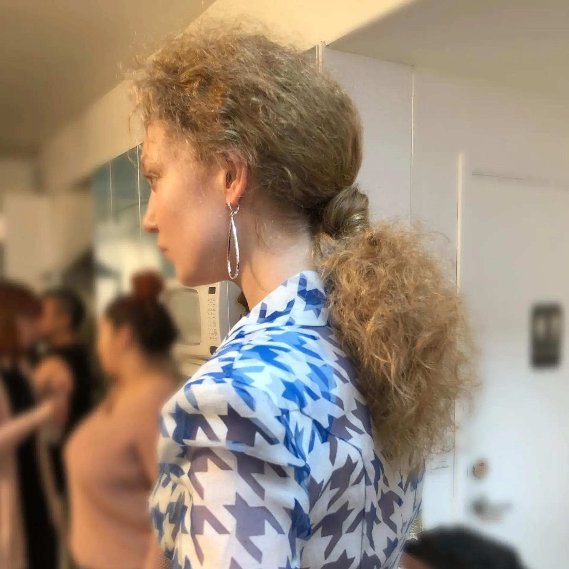 A low ponytail gathered at the nape with hair wrapped around the base and brushed-out crimped texture. 1