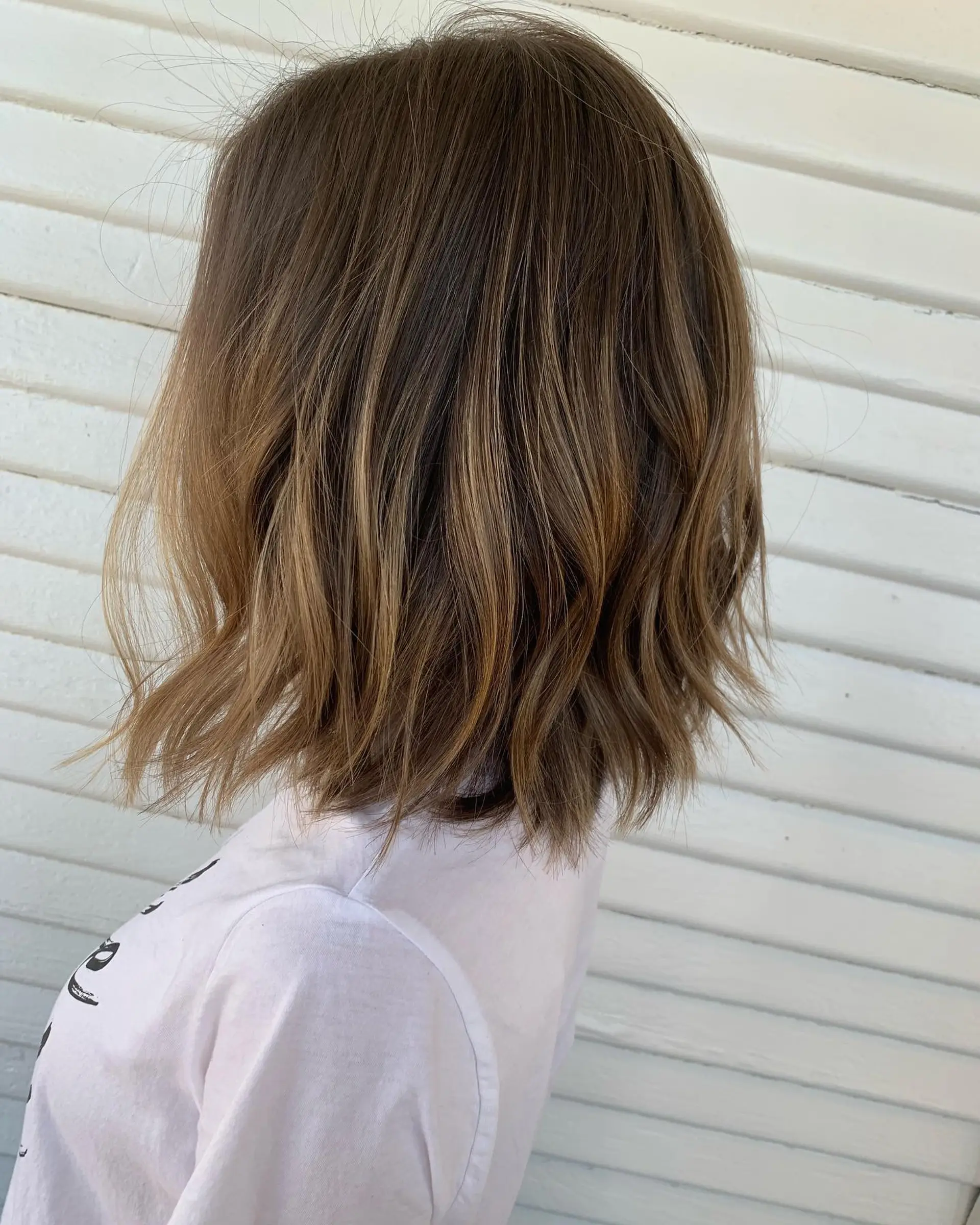 A textured shoulder-length lob styled with effortless beachy waves and dimensional caramel highlights. 1