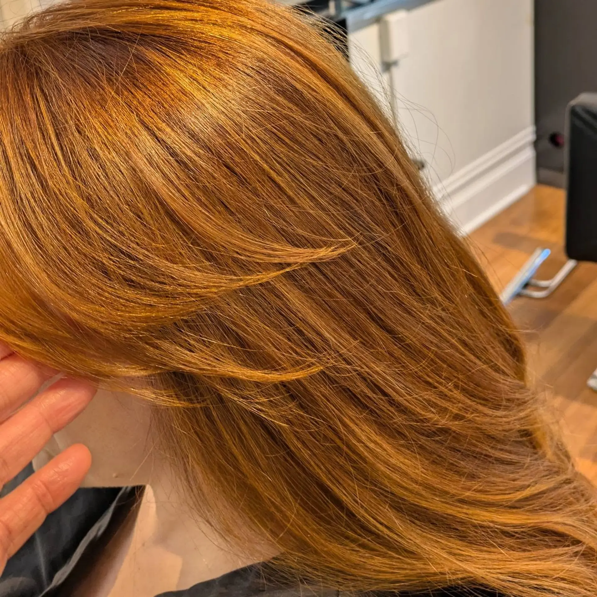 Long warm copper hair cut with soft, feathered face-framing layers and styled into a sleek blowout. 1