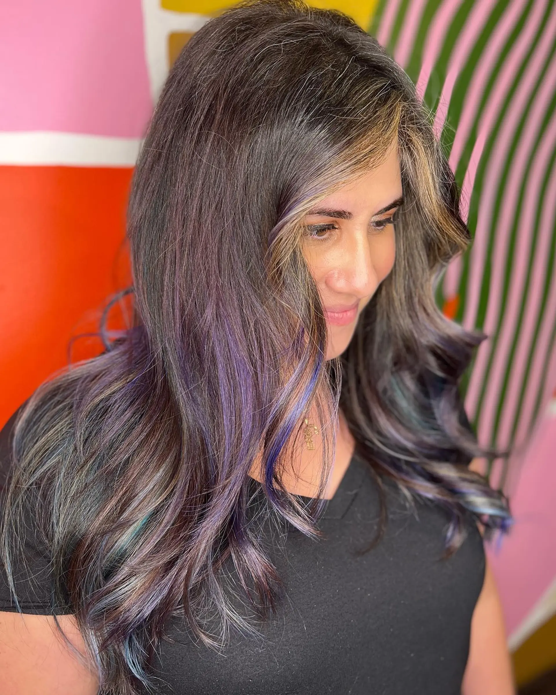 Long dark wavy hair featuring subtle purple and teal oil slick highlights with a warm blonde face-framing accent. 1