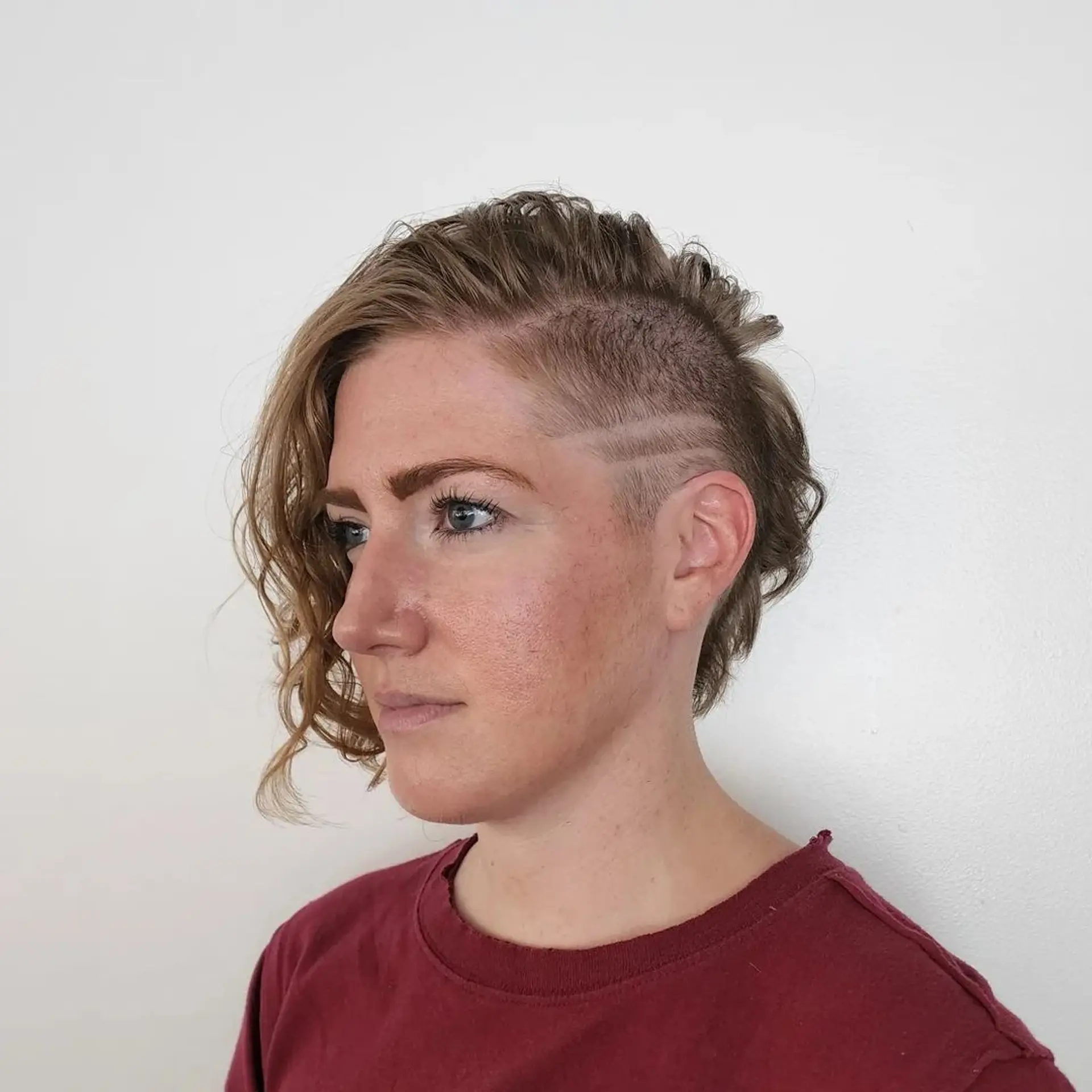 Daring combination of shaved sides with two line designs and longer wavy strands on top for a bold, modern effect. 2