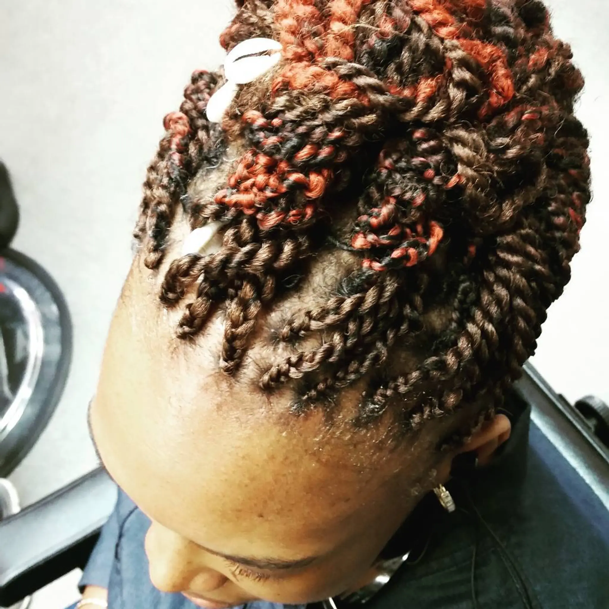 A short twist out hairstyle with brown and copper tones, accented with shell accessories.