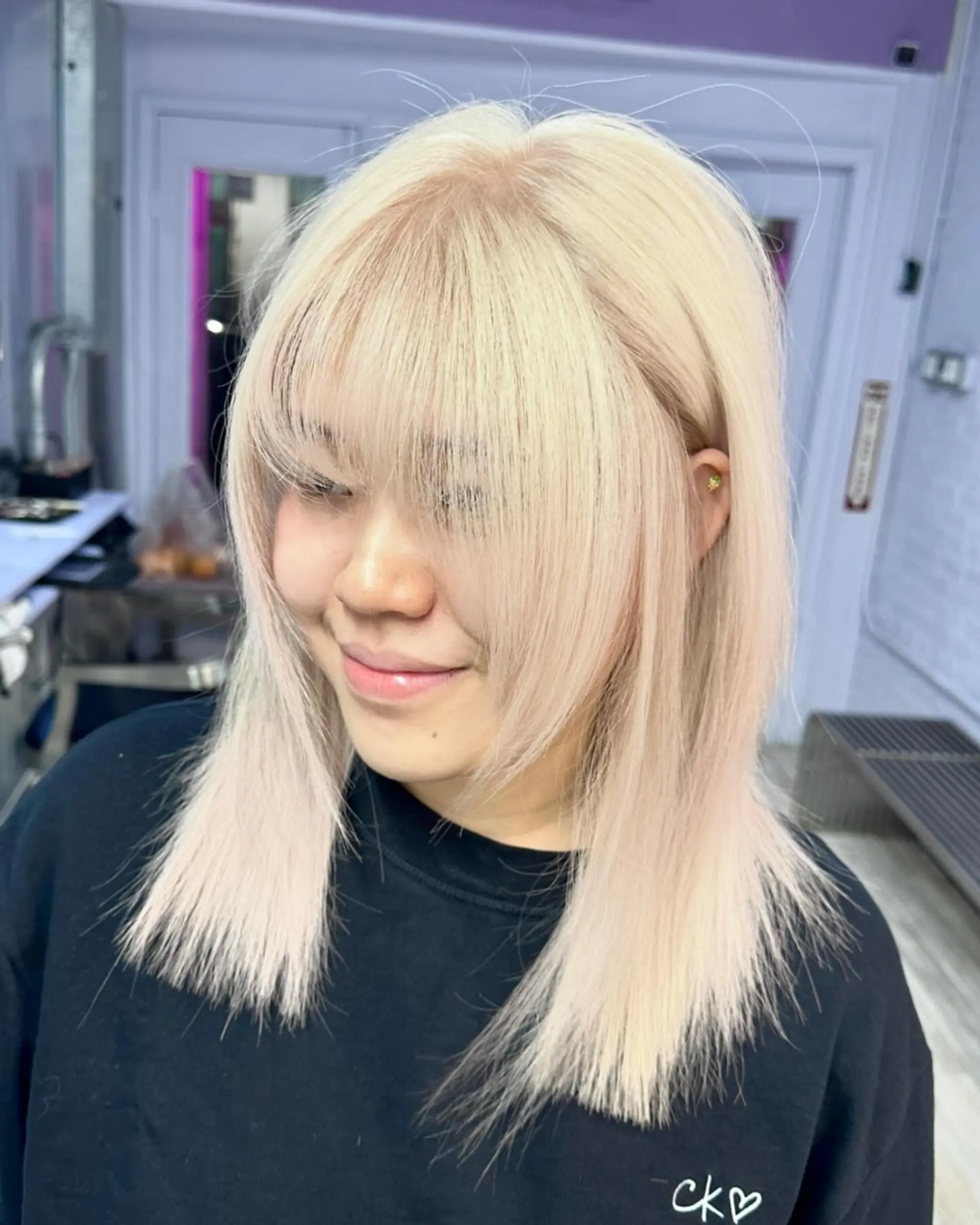 A sleek, medium-length platinum blonde hairstyle with full, straight-across bangs and face-framing layers. The straight hair has a soft, shiny finish and a light, airy texture, creating a modern and chic look. 1