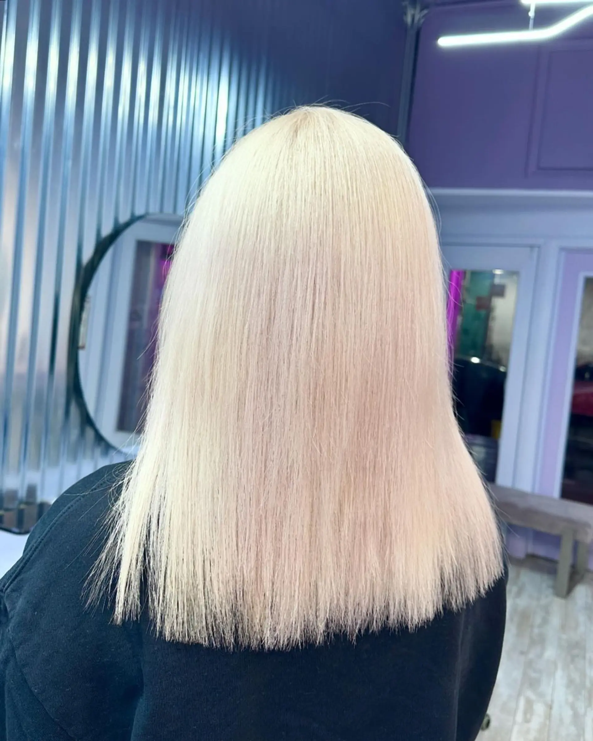 A sleek, medium-length platinum blonde hairstyle with full, straight-across bangs and face-framing layers. The straight hair has a soft, shiny finish and a light, airy texture, creating a modern and chic look. 3