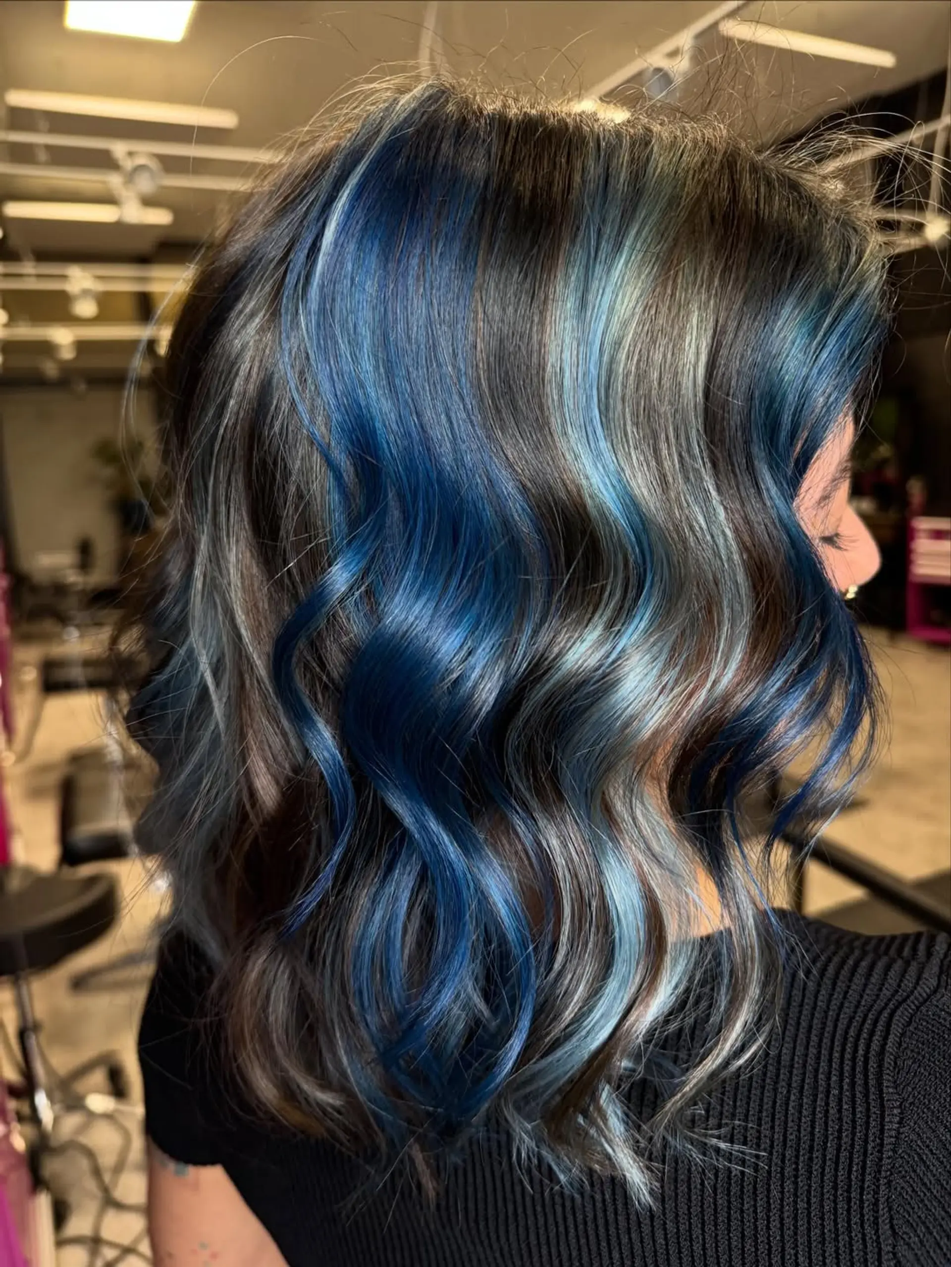 A stunning multi-tonal wavy lob, showcasing a rich blend of deep ocean blues, icy light blues, and silver highlights over a darker base. The medium-length cut is styled with soft, defined waves for a chic and playful look. 1