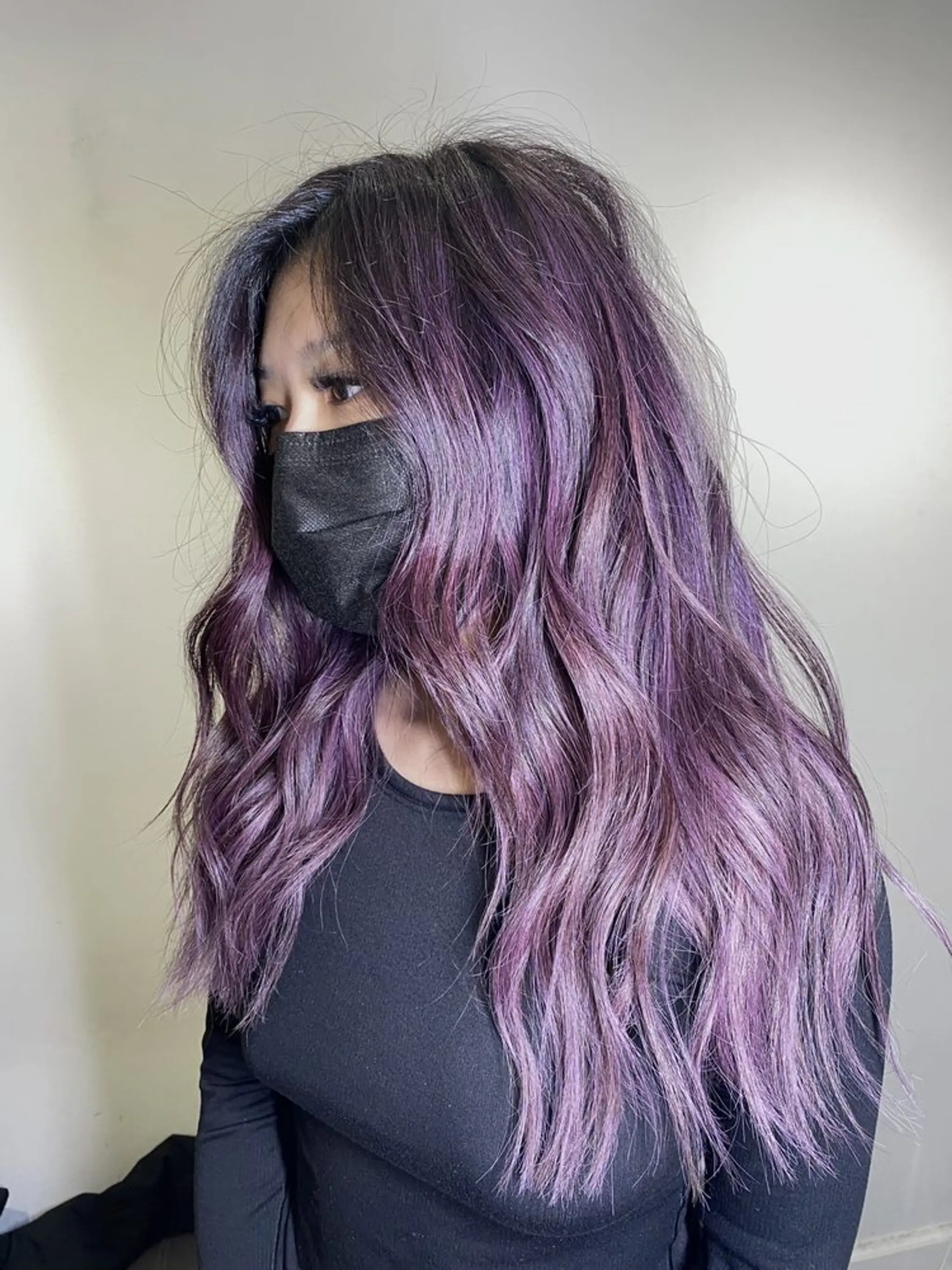 A long, wavy hairstyle with vibrant purple tones and lavender highlights. The hair is layered, providing depth and dimension to the waves, enhancing the luxurious and voluminous appearance.