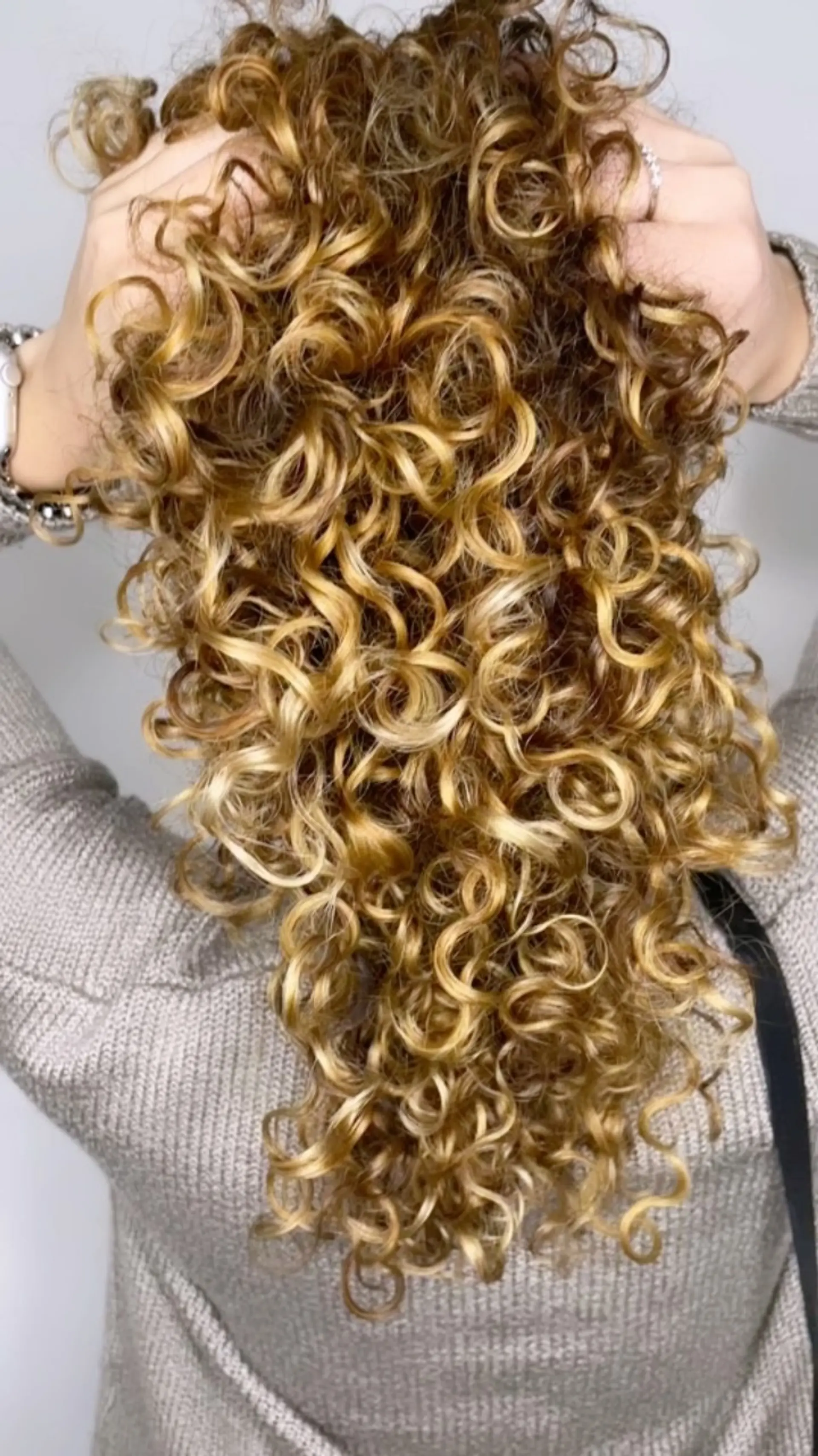 Medium-length tight ringlet curls illuminated with multi-dimensional warm golden blonde and caramel highlights. 1