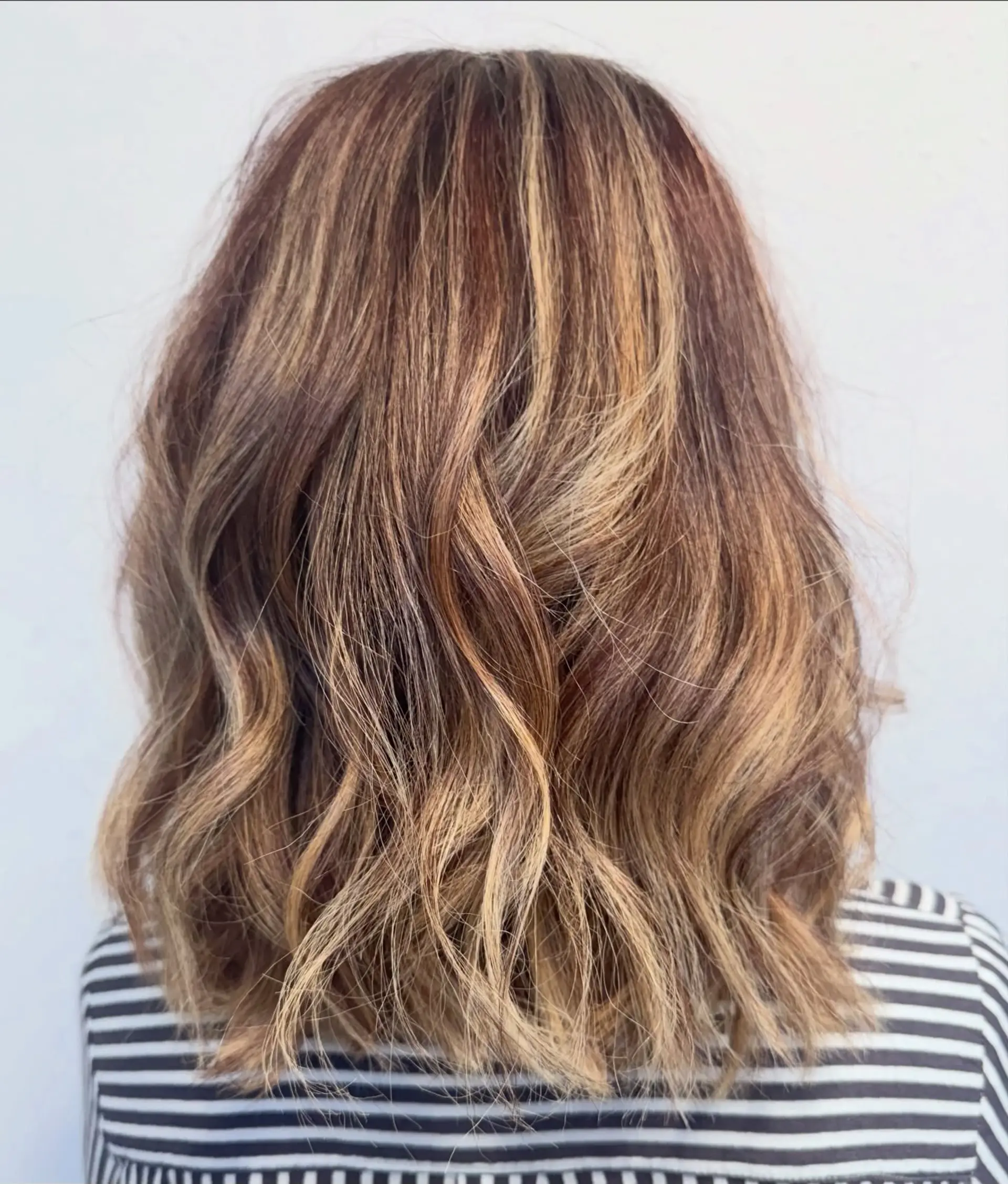 Shoulder-length textured cut styled in loose, lived-in waves with multi-tonal caramel and warm honey balayage highlights. 1