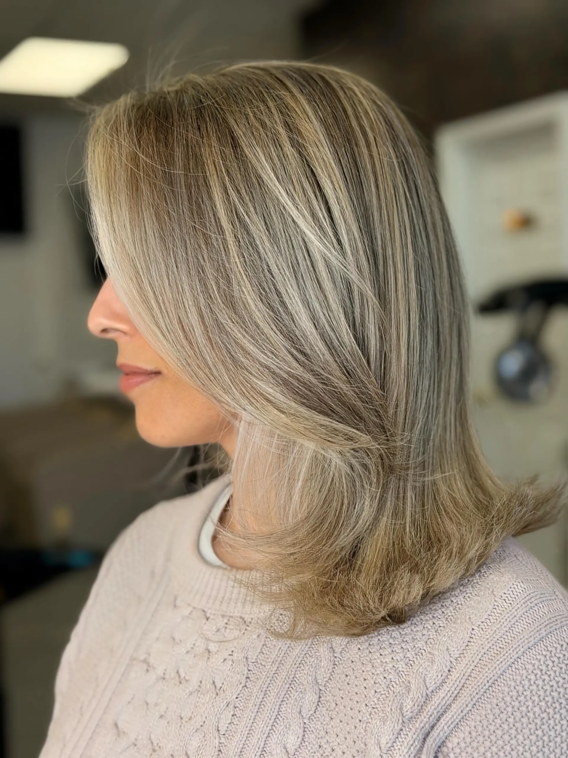 Medium-length layered haircut featuring fine ash blonde highlights and a smooth blowout with softly flipped-out ends. 1