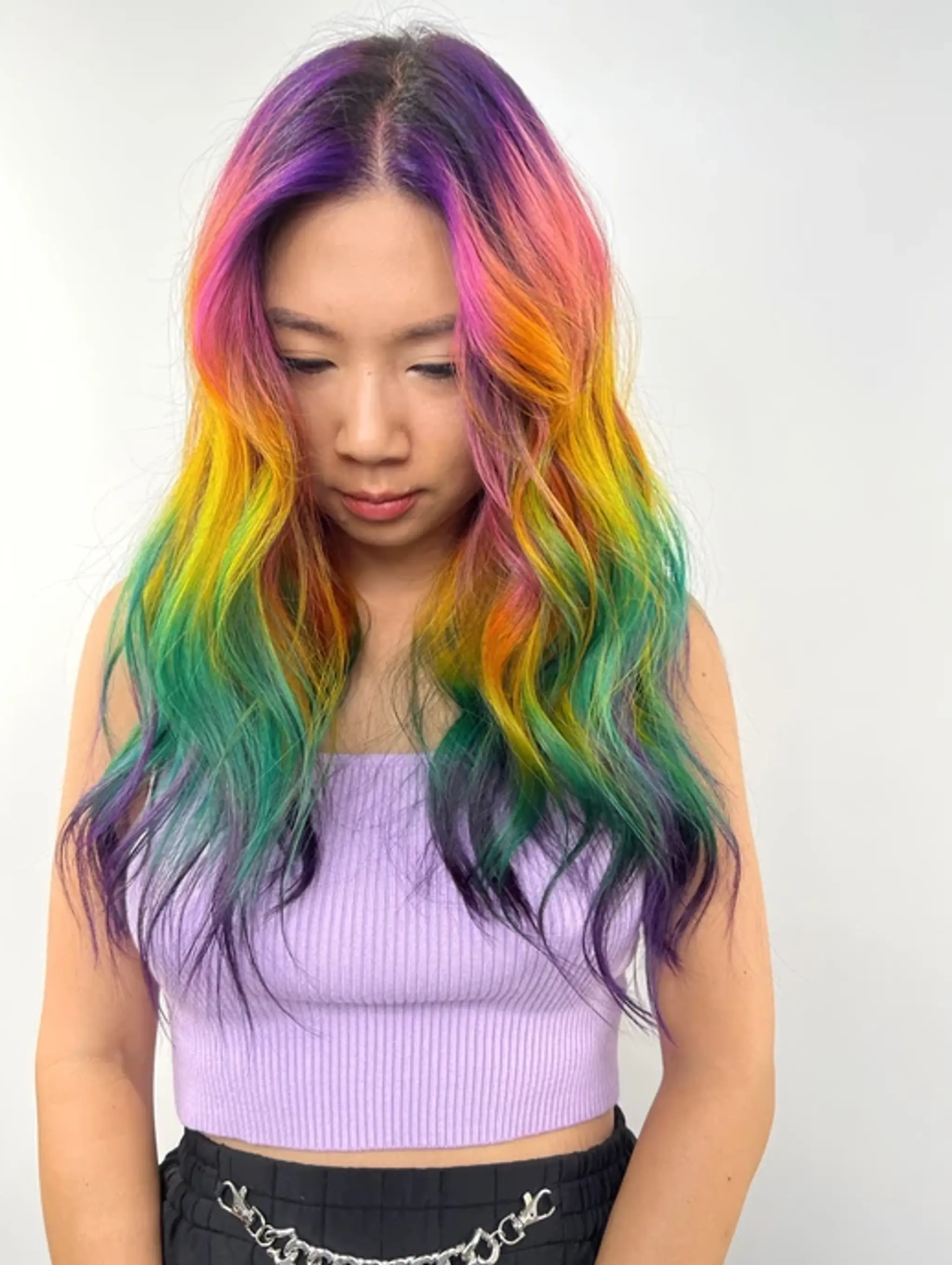 Vibrant, wavy hair cascading down in a seamless gradient of purple, pink, yellow, green, and blue, creating a prismatic effect.