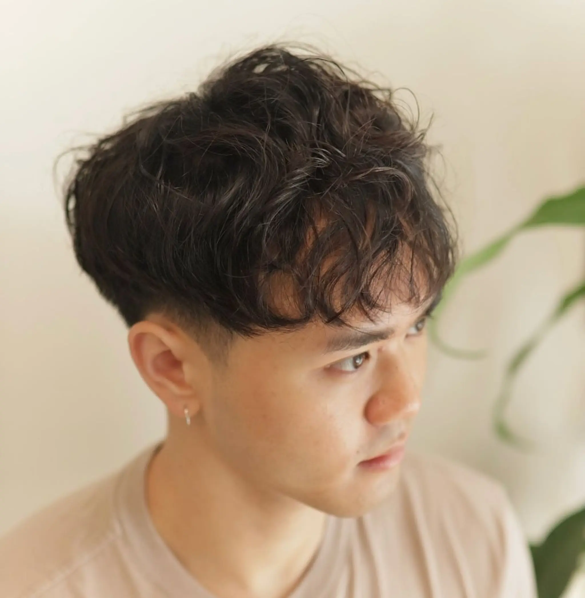A trendy undercut featuring naturally wavy, black hair cut short with a longer, textured top and a light fringe for a casual, effortless look.