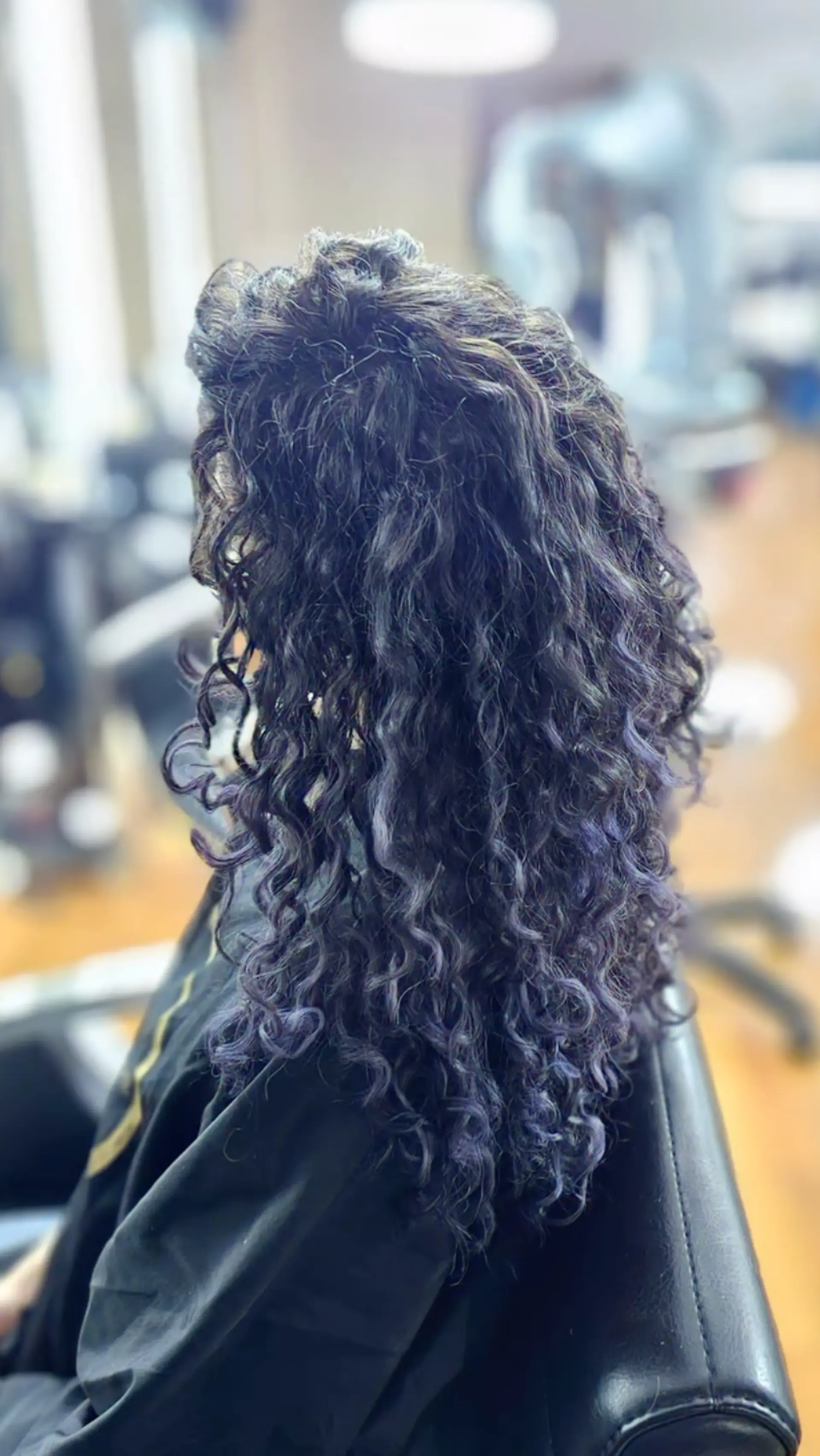 The hair features medium-length defined curls with a natural volume, transitioning from a black base color to vibrant purple highlights, forming a root-to-end gradient. 2