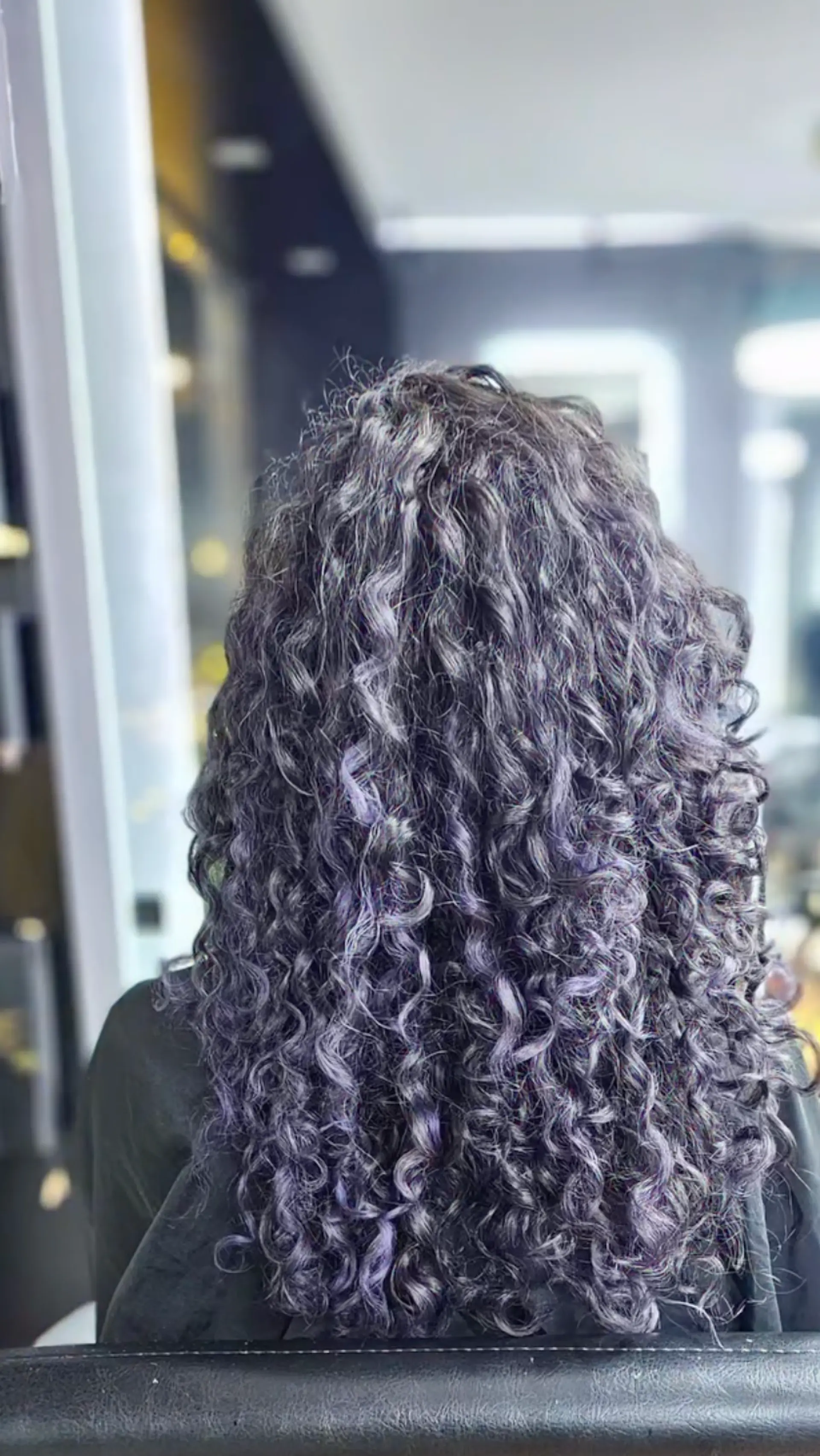 The hair features medium-length defined curls with a natural volume, transitioning from a black base color to vibrant purple highlights, forming a root-to-end gradient. 3