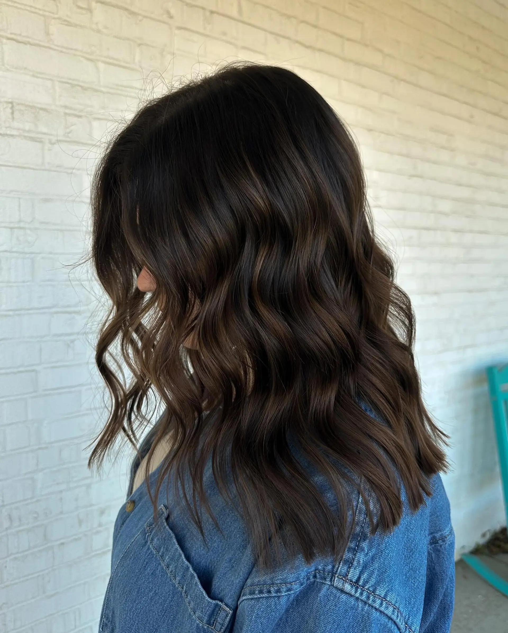 Rich espresso brunette hair cut to medium length and styled into glossy, defined waves with subtle warm dimension. 1