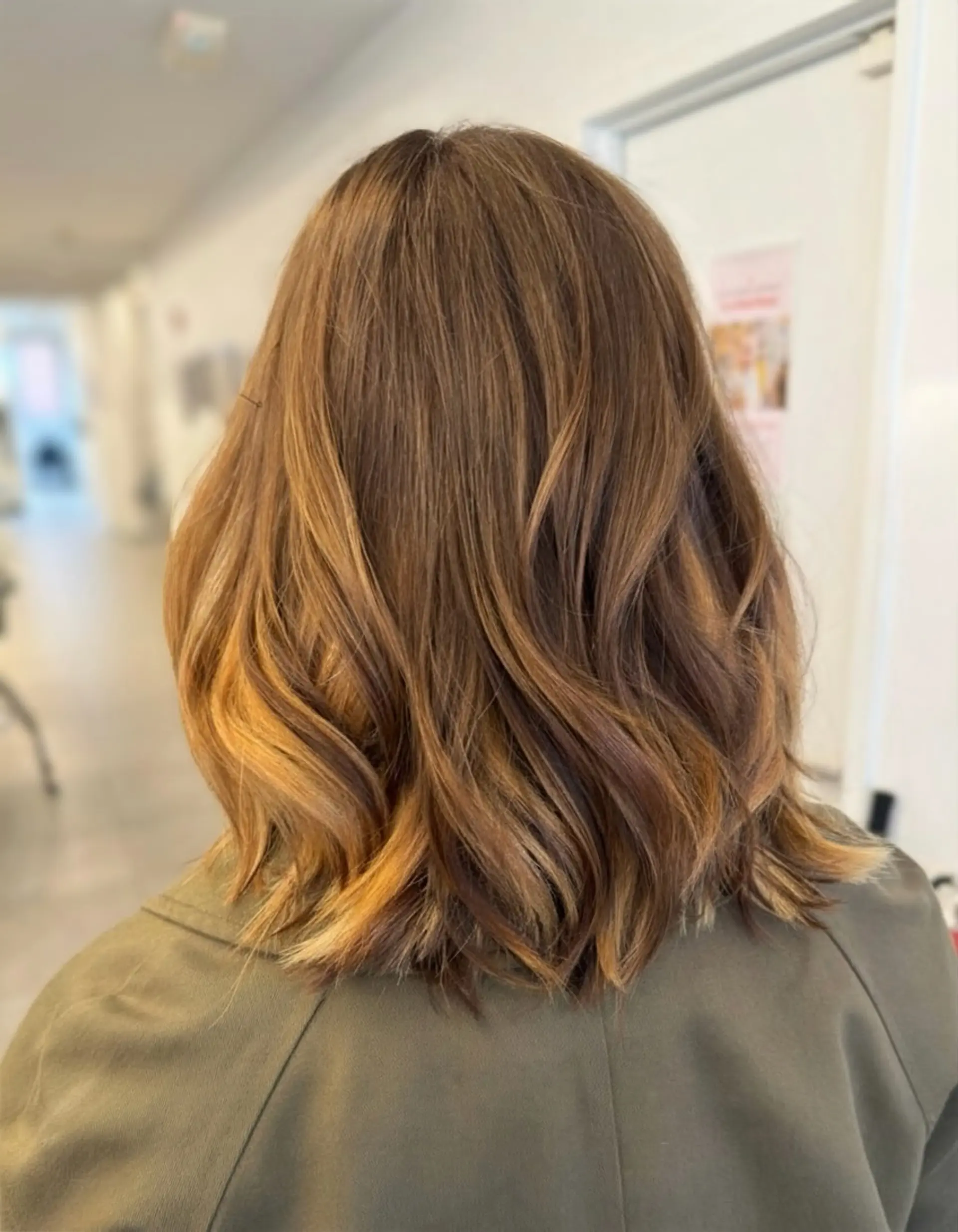 A textured medium-length lob featuring warm caramel balayage highlights and gentle, soft waves. 1