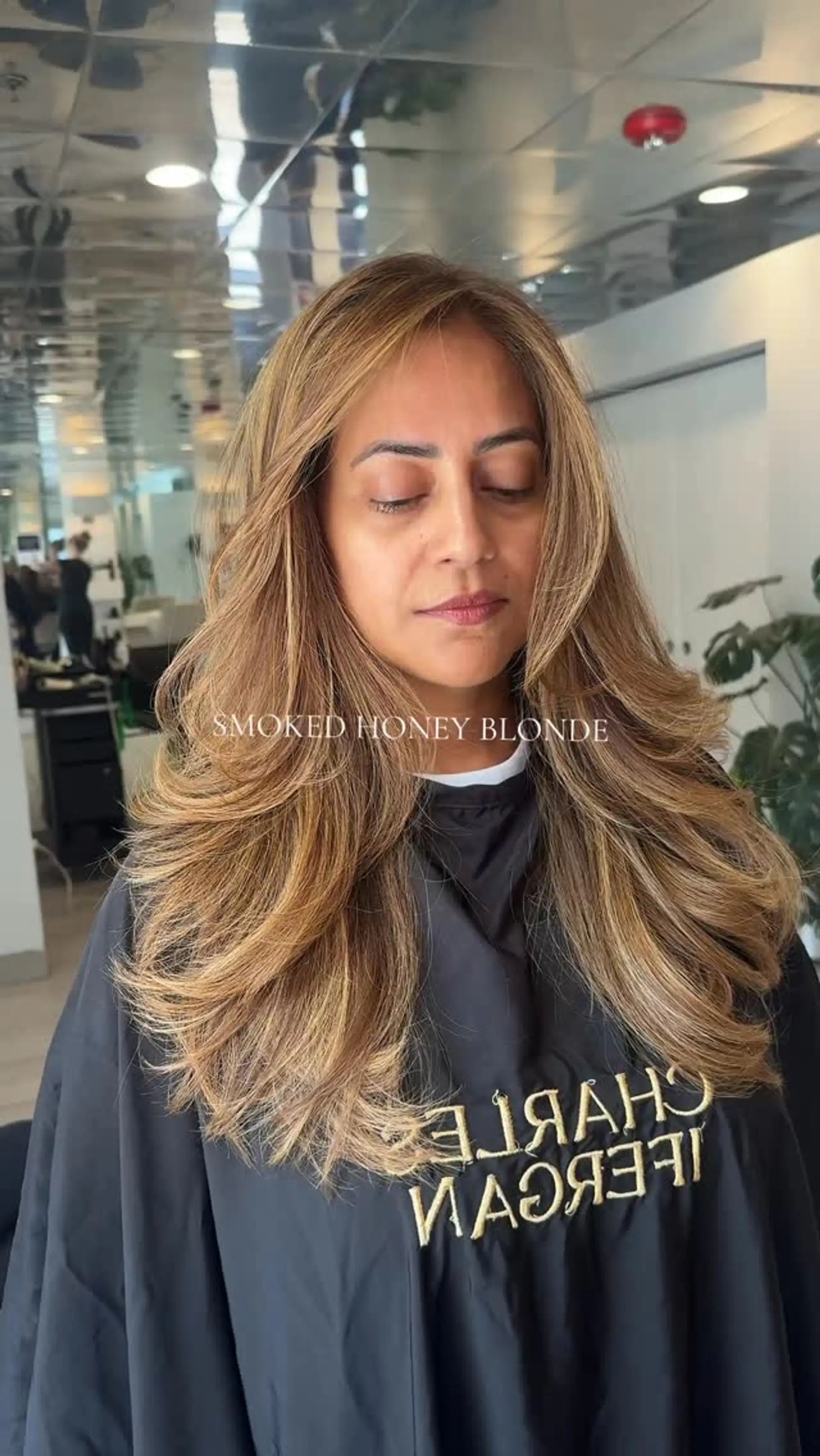 Long layered hair with warm smoked honey blonde tones, styled in a bouncy, feathered blowout. 1