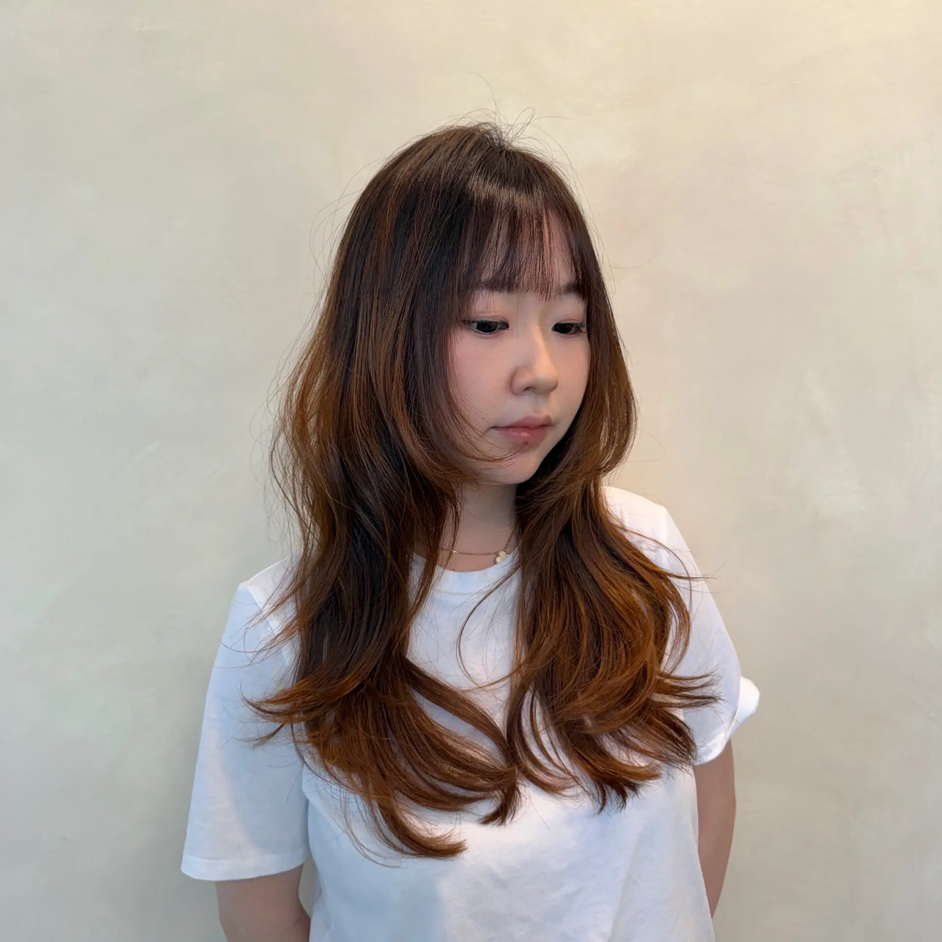 Long layered haircut with delicate see-through fringe bangs and face-framing ends styled with soft outward waves. 1