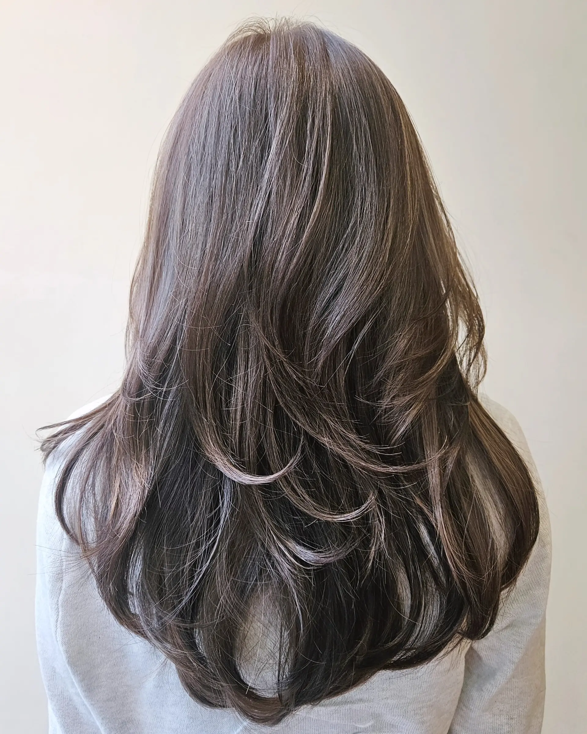 Long ash-toned brown hair styled with cascading layers and soft, curled ends. 1