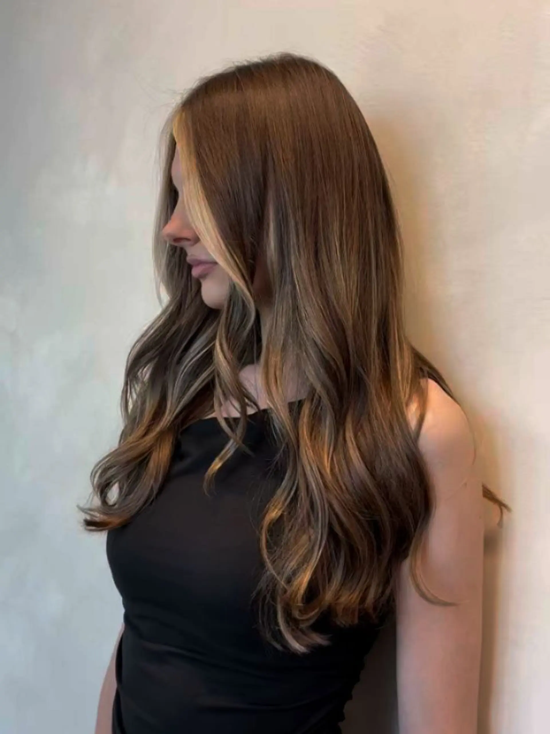Long brown hair cut with soft cascading layers and styled in gentle waves, accented with bright blonde face-framing highlights. 1