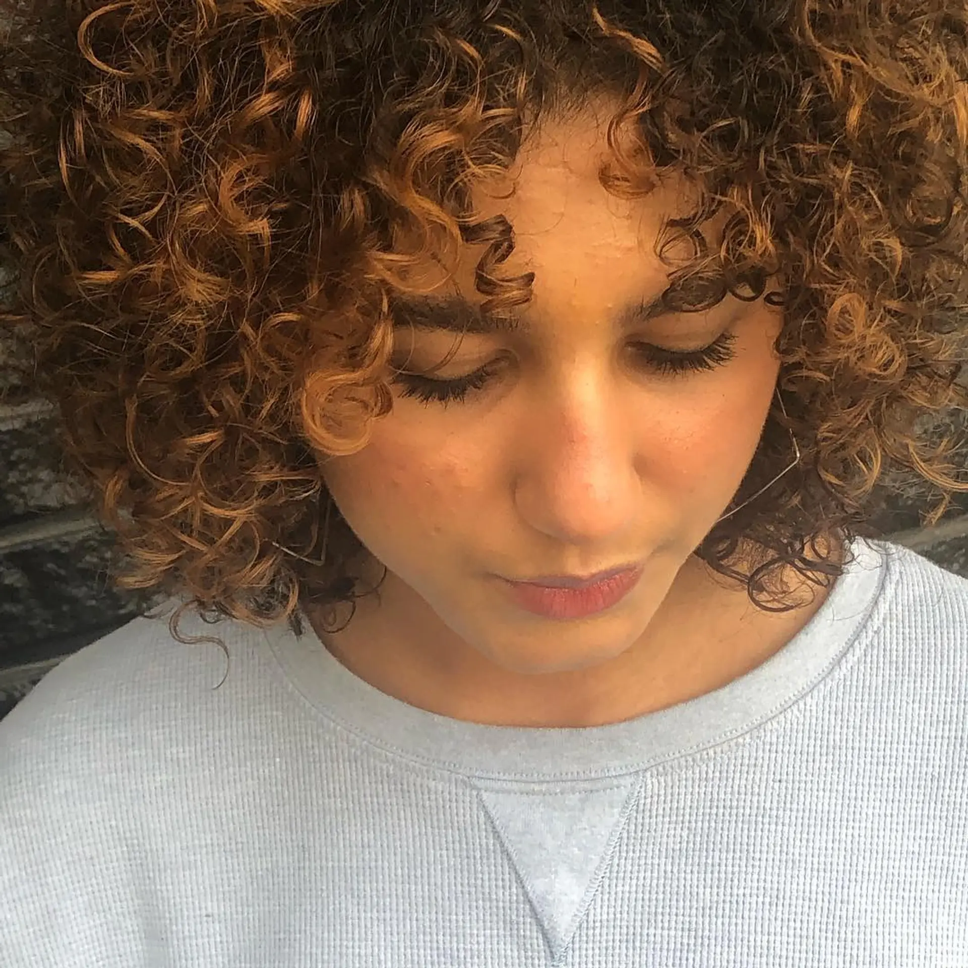 A shaped curly bob featuring rounded layers, soft curly fringe, and warm caramel dimensional highlights throughout tight, defined ringlets. 1