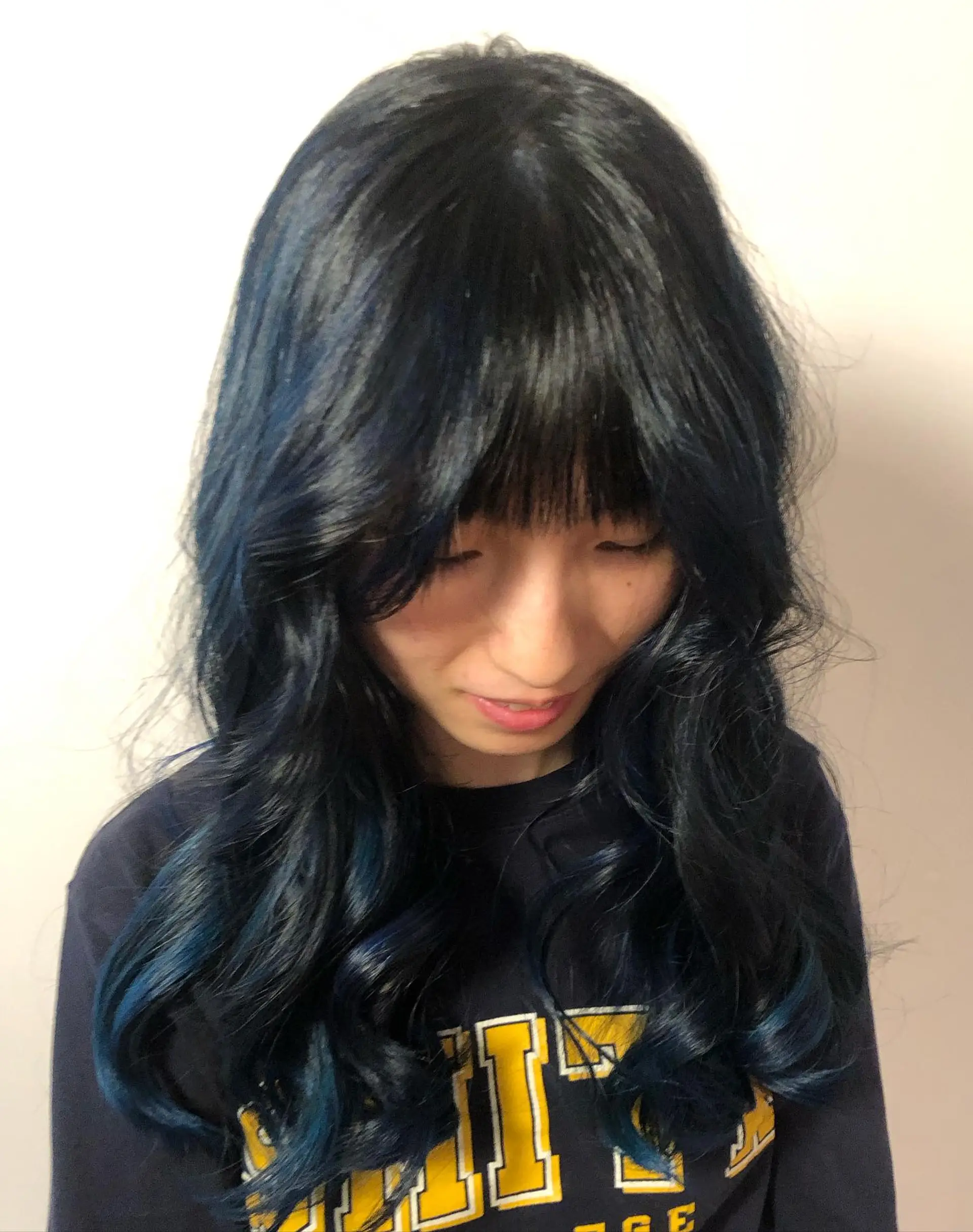 Deep midnight blue dyed hair styled with soft, cascading waves and straight brow-grazing fringe bangs. 1