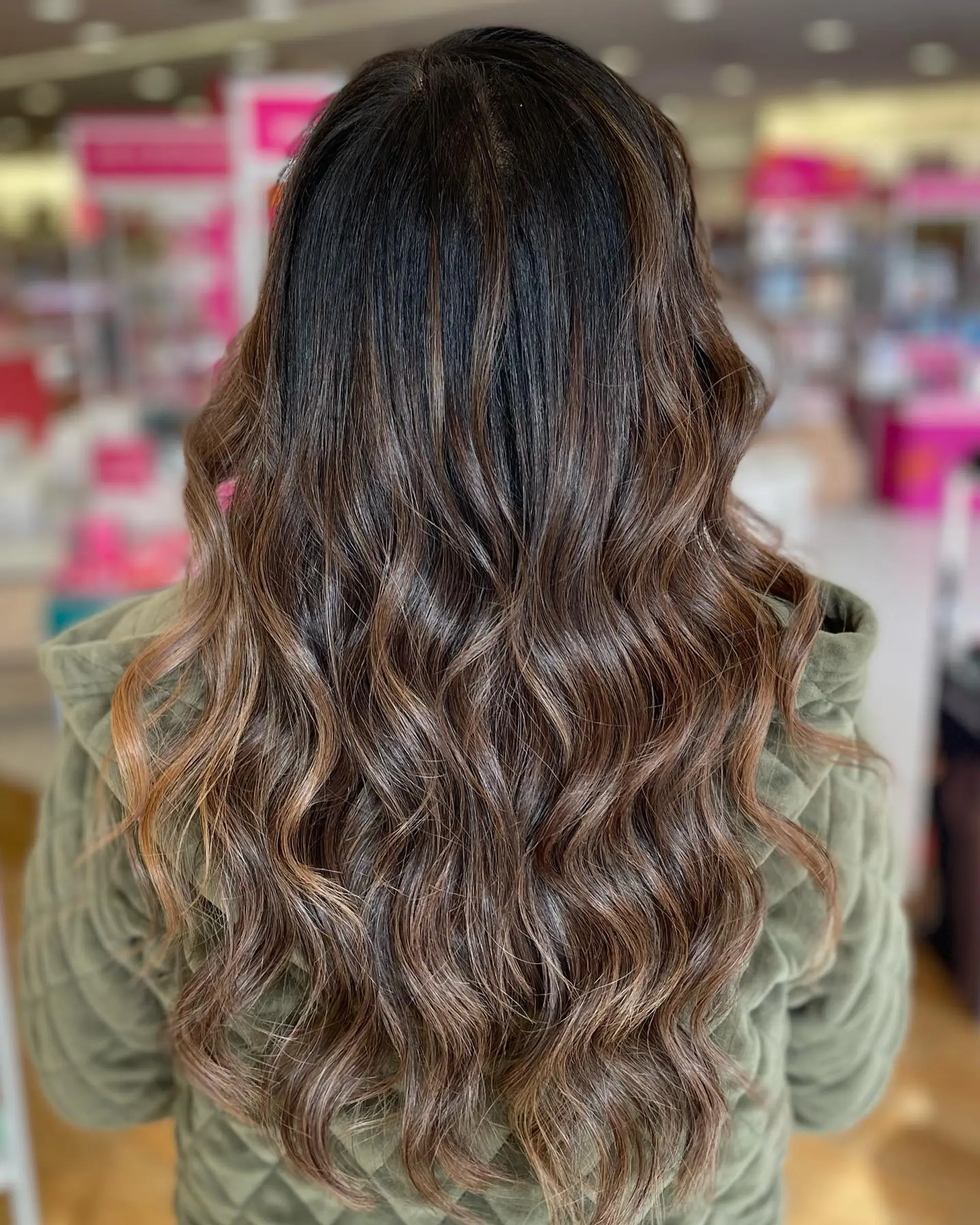 Long dark brown hair featuring blended caramel balayage highlights styled in soft, cascading waves. 1