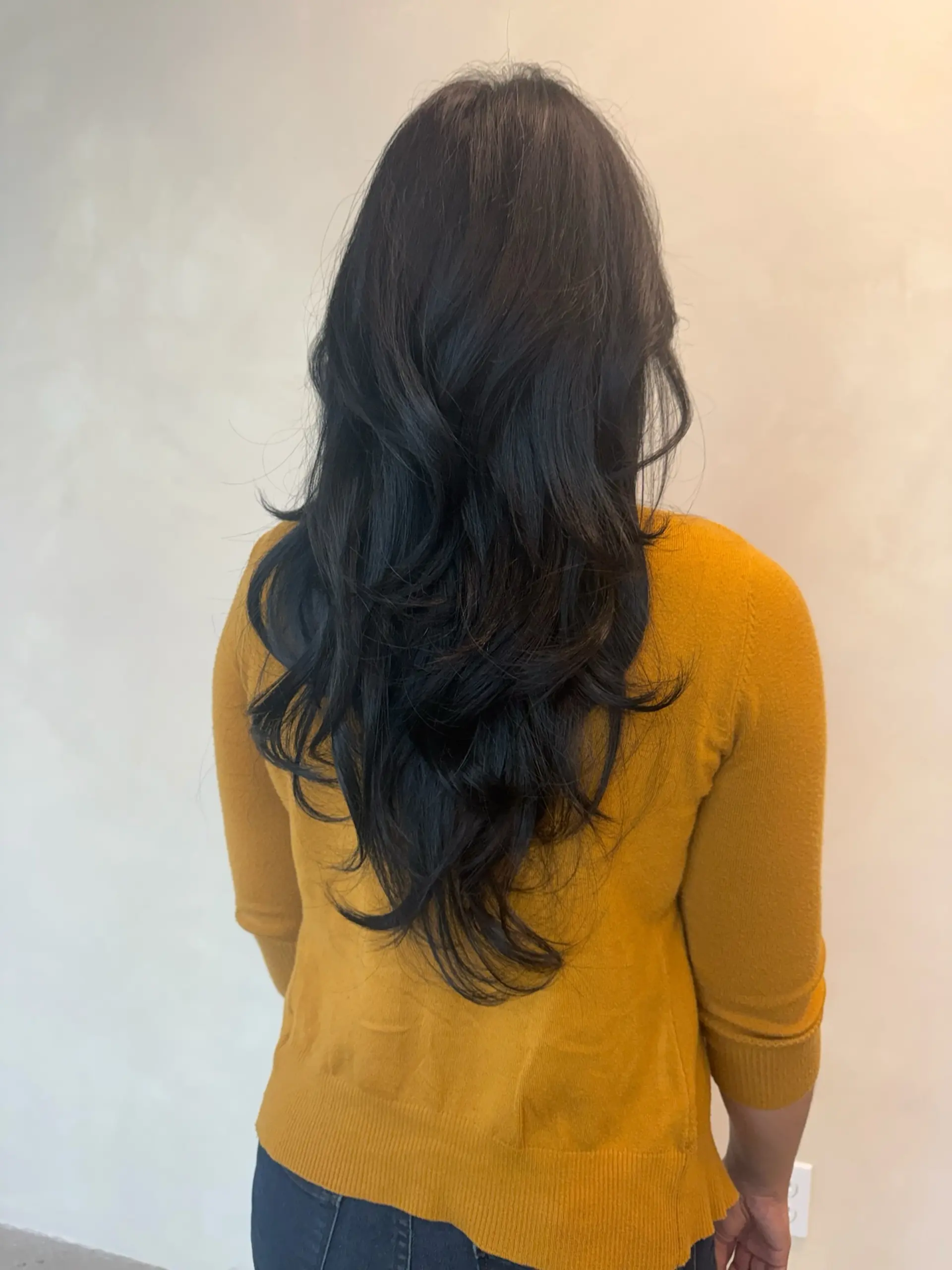 Long black layered hair styled with flicked-out ends and voluminous body waves. 1