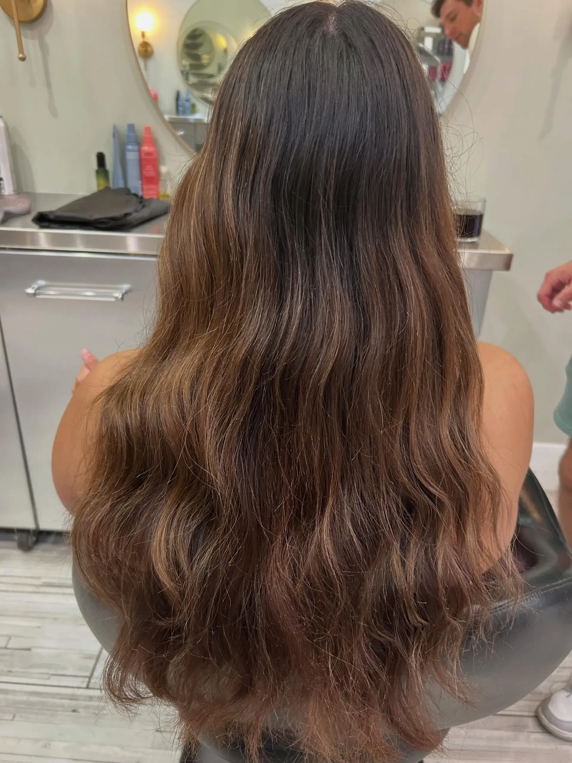 Long, dimensional brunette hair styled in soft natural waves with subtle lighter accents throughout. 1