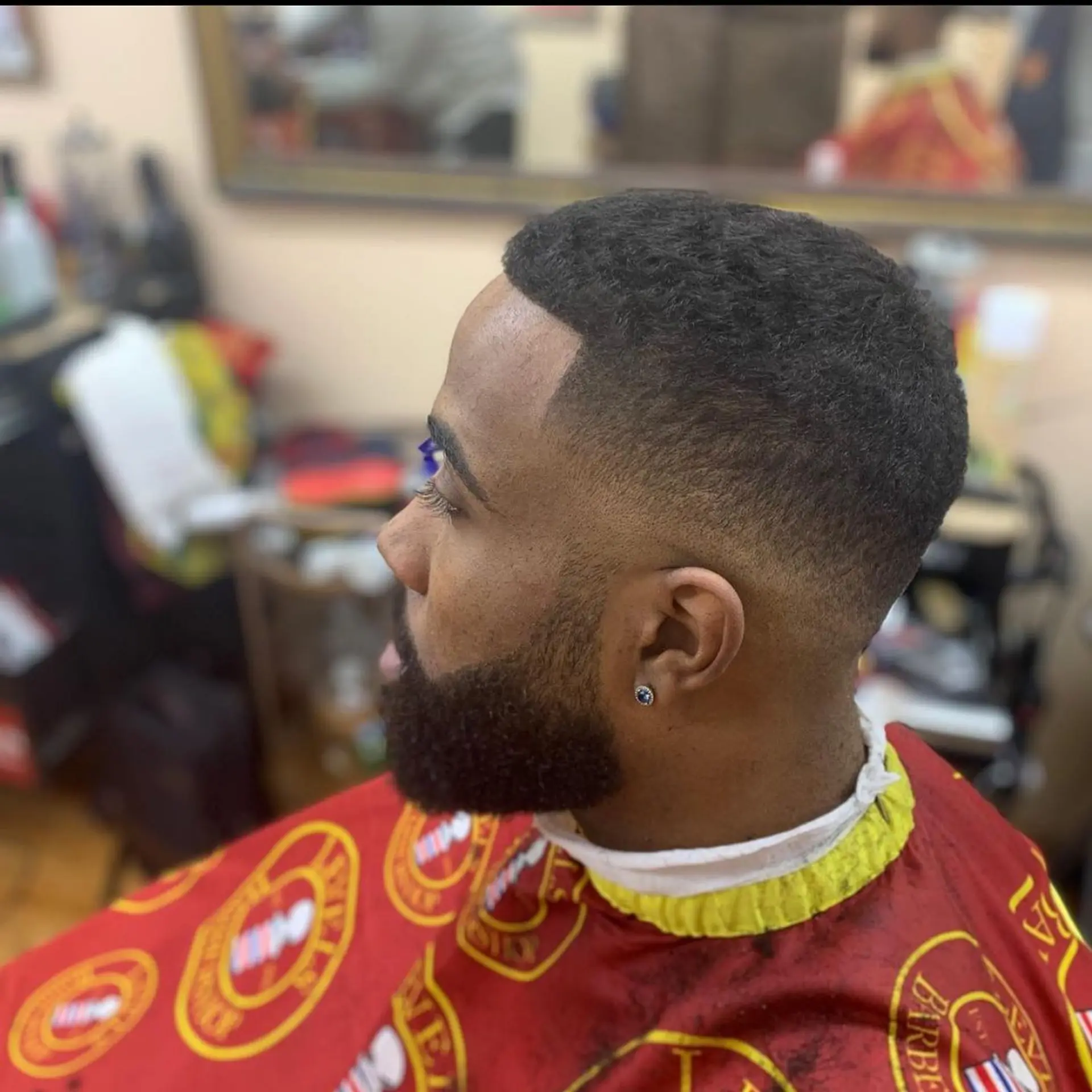 A precise mid fade haircut paired with a sharp line-up and a cleanly shaped full beard. 1