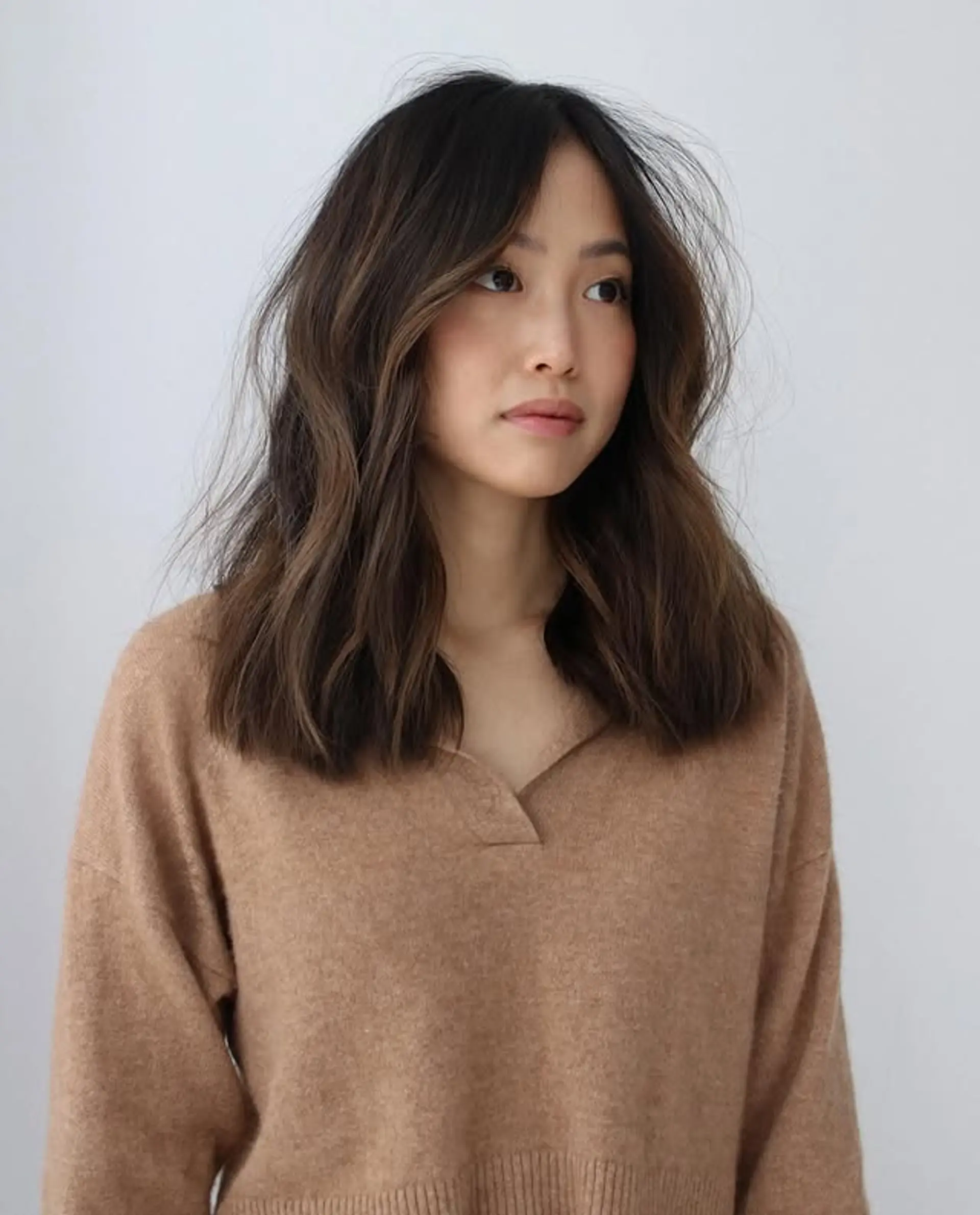 A medium length wavy hairstyle with face-framing layers, featuring a blend of dark brown and bronze tones. 1