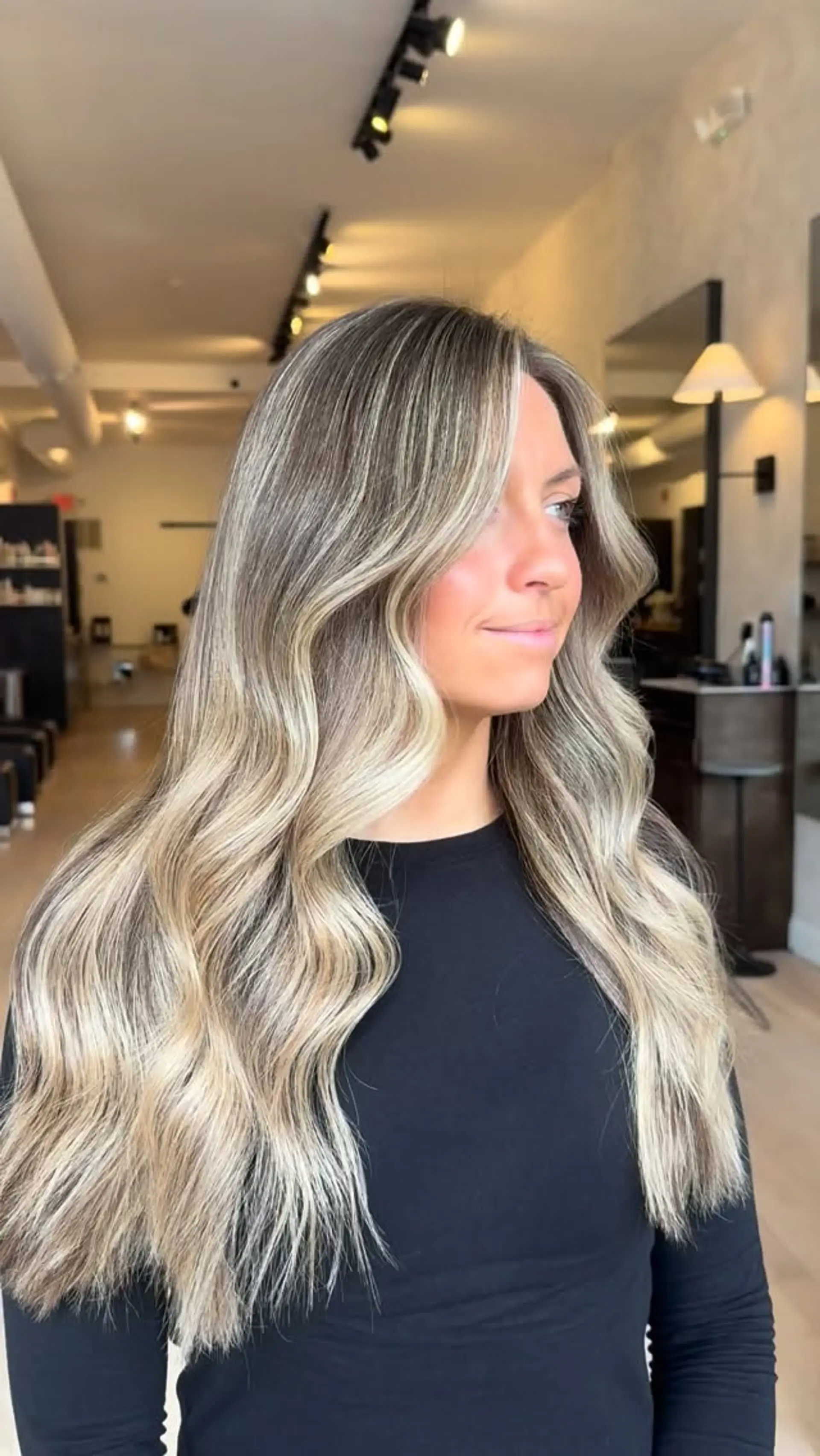 Long dimensional ash blonde hair styled in soft, loose waves with face-framing highlights. 1