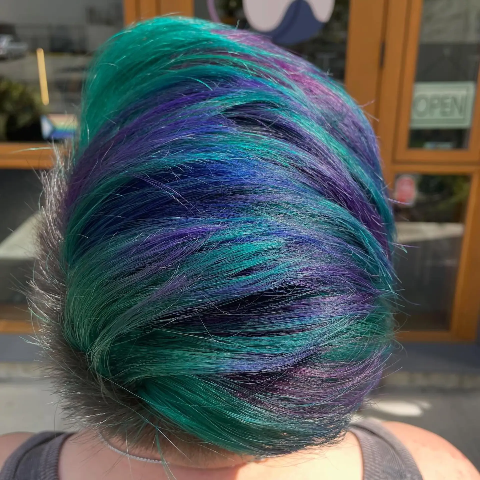 A short, textured pixie cut styled to the side, featuring multi-toned vivid color with vibrant teal, indigo blue, and purple tones. 1