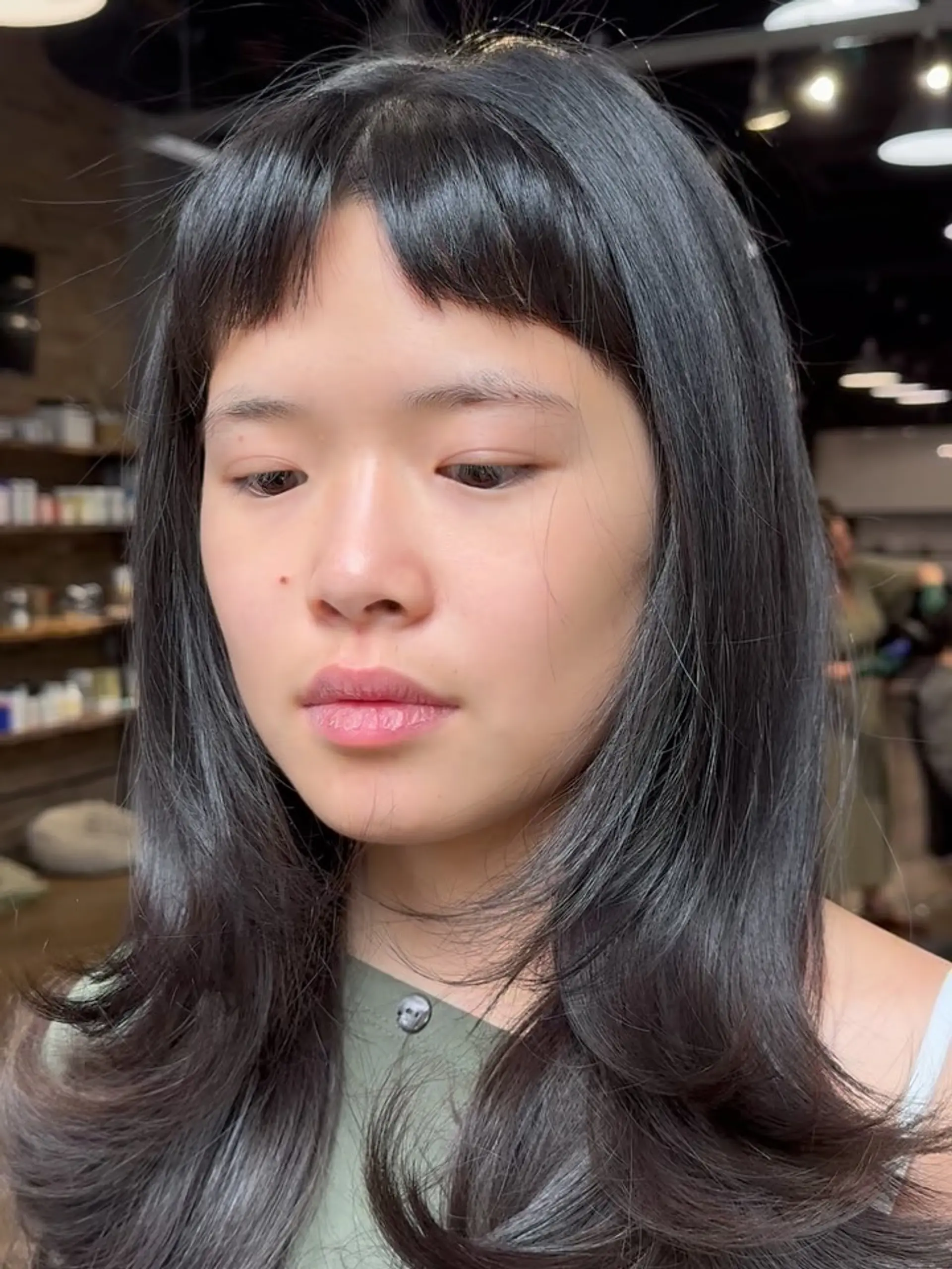 Medium-length dark hair styled with textured micro baby bangs and soft, face-framing layered waves. 1