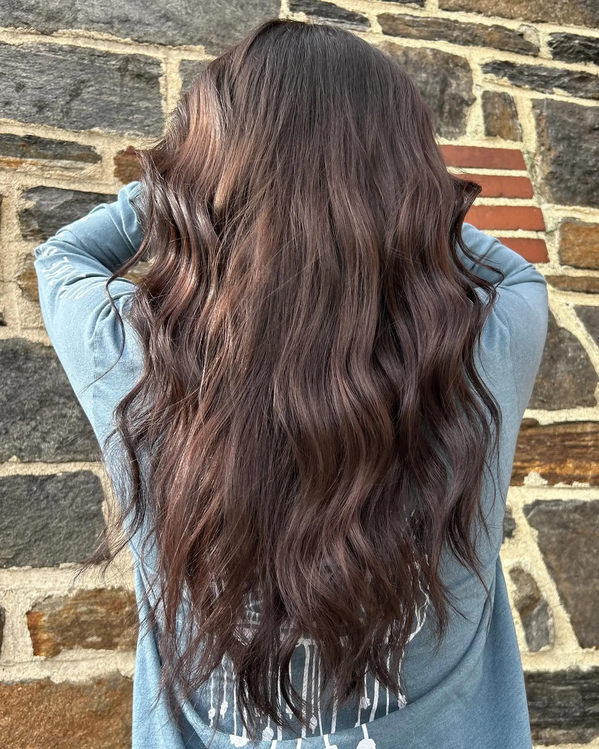 Long, glossy rich brunette hair styled with soft, loose waves cascading down the back. 1