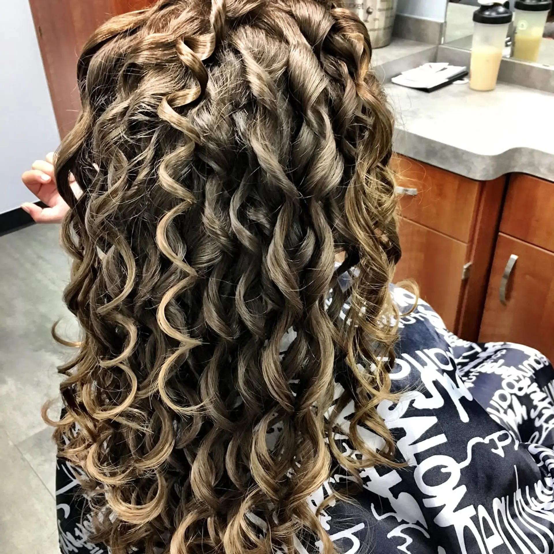 Long brown hair styled into glossy, defined spiral curls with delicate caramel highlights throughout. 1