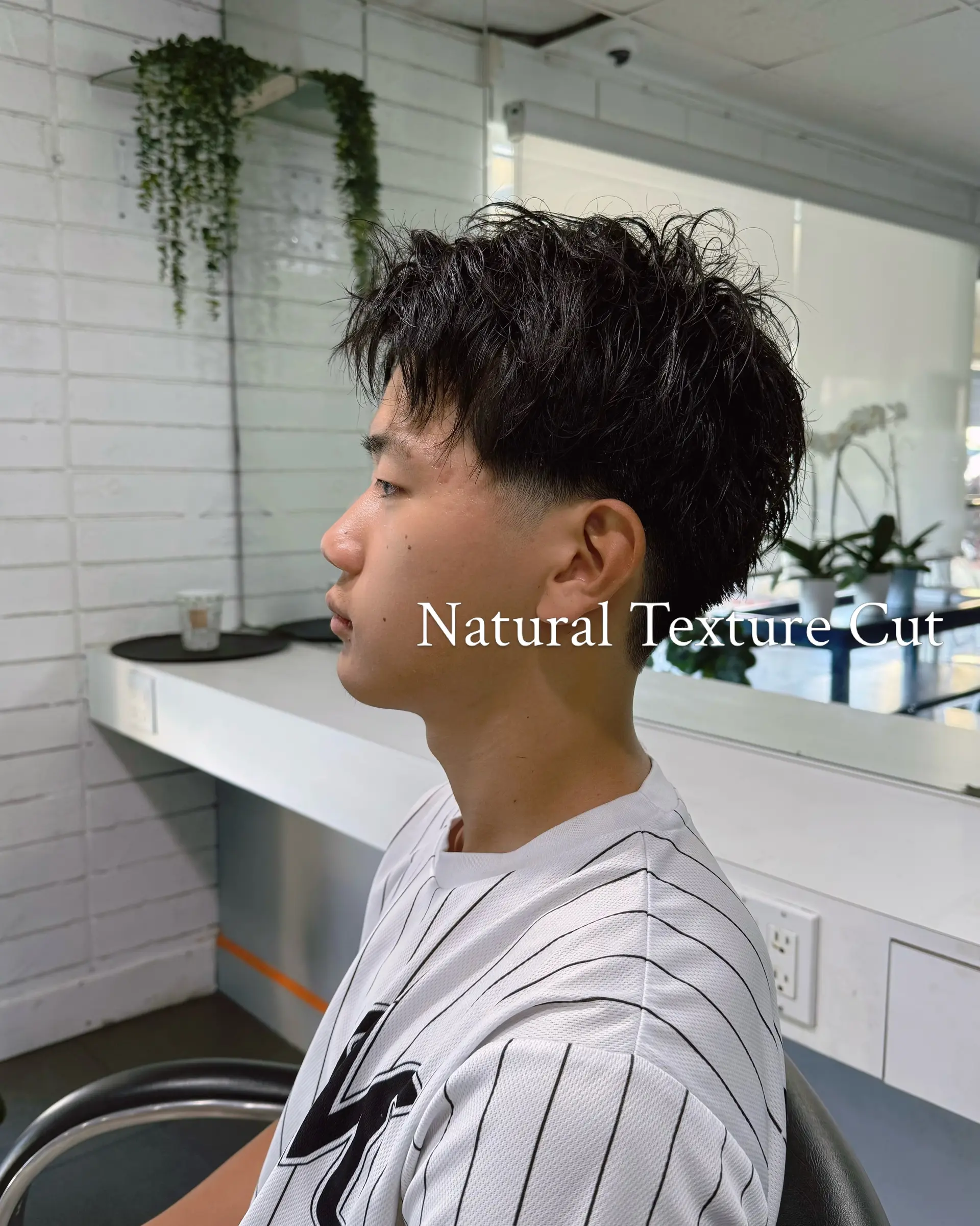 A short men's haircut featuring natural textured layers on top and a clean, soft low taper around the temples and neckline. 1