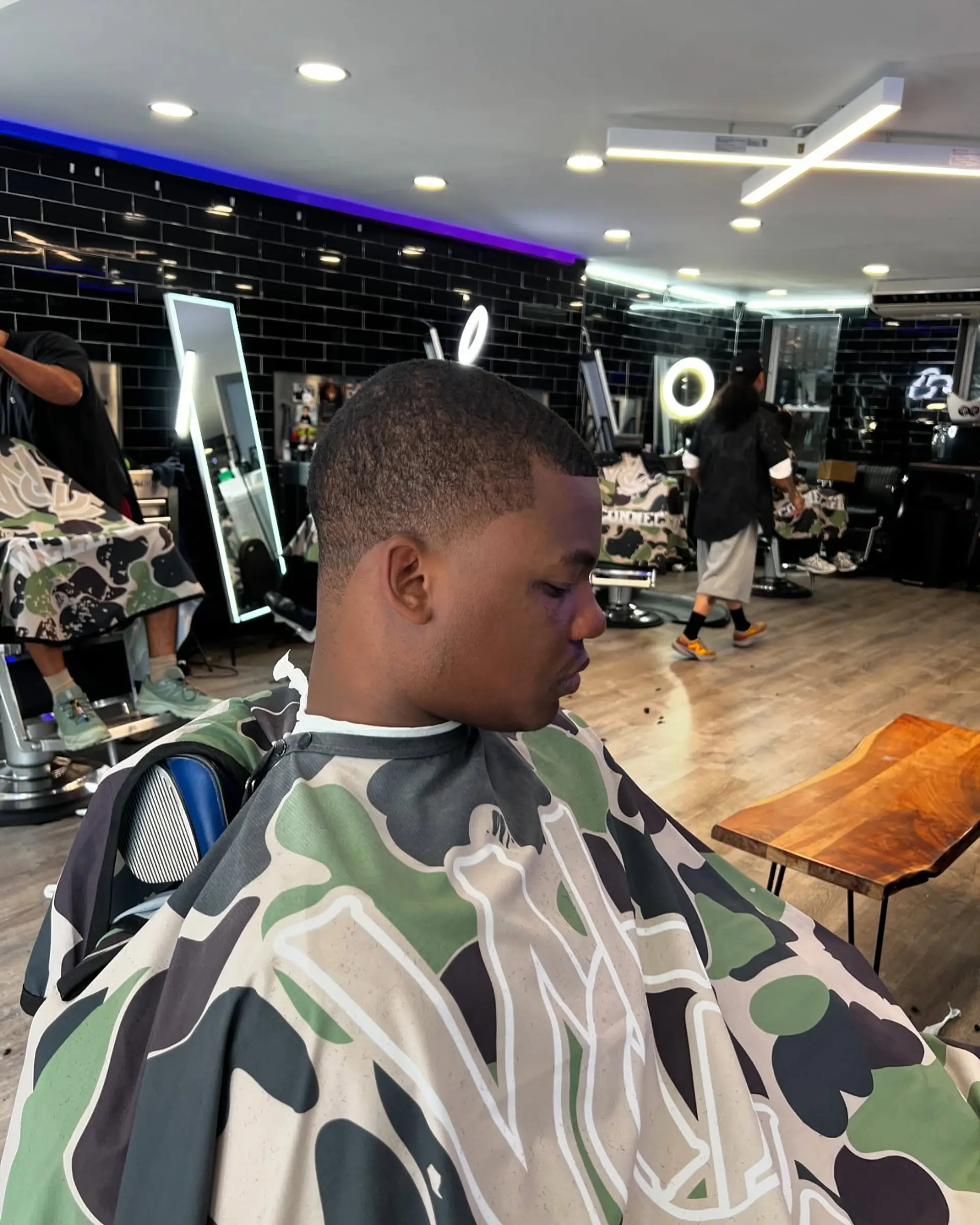 A clean short buzz cut styled with a sharp hairline edge-up and a subtle low taper fade around the sideburns and neckline. 1