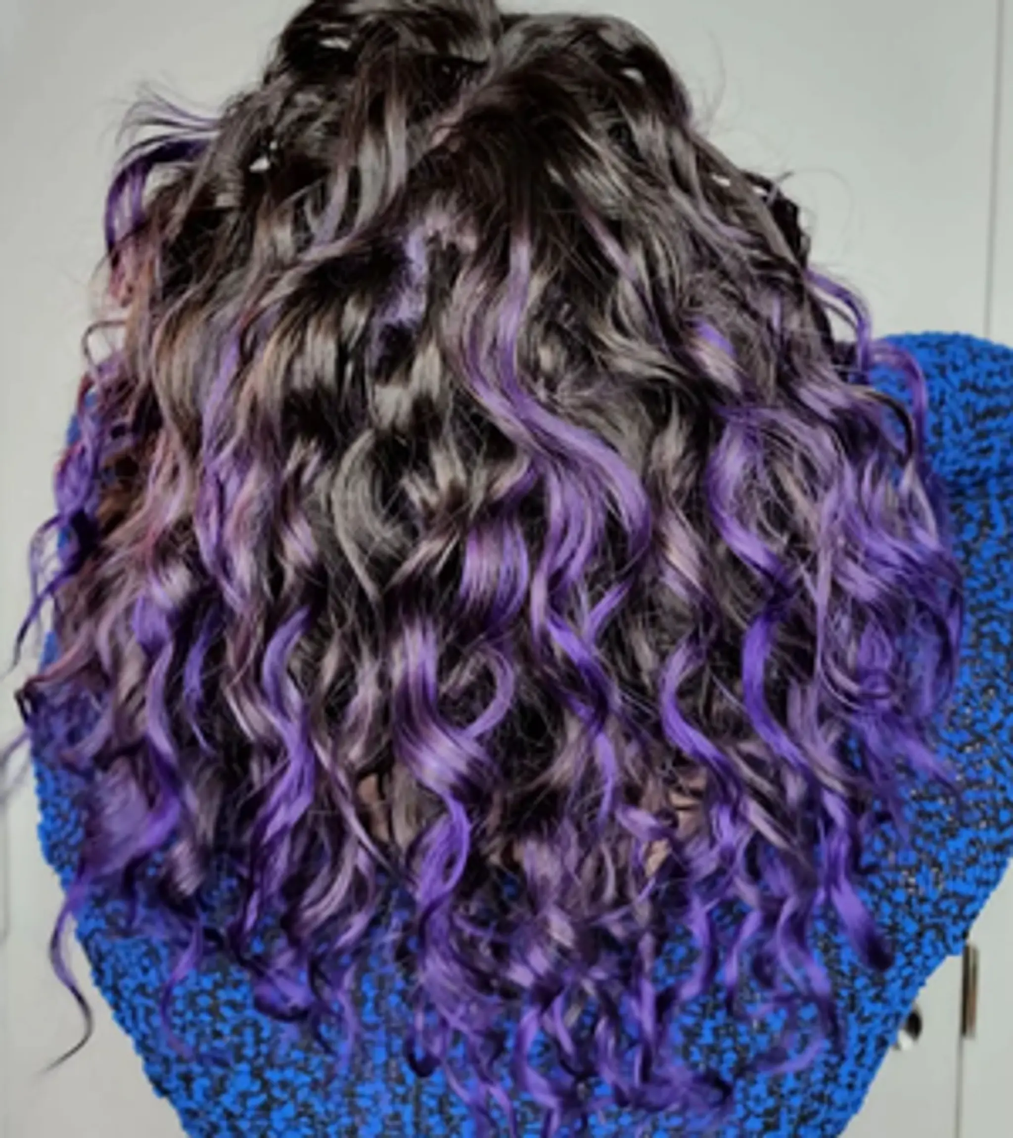Medium-length, curly hair with a deep black base color and striking purple highlights, layered for added volume and texture.