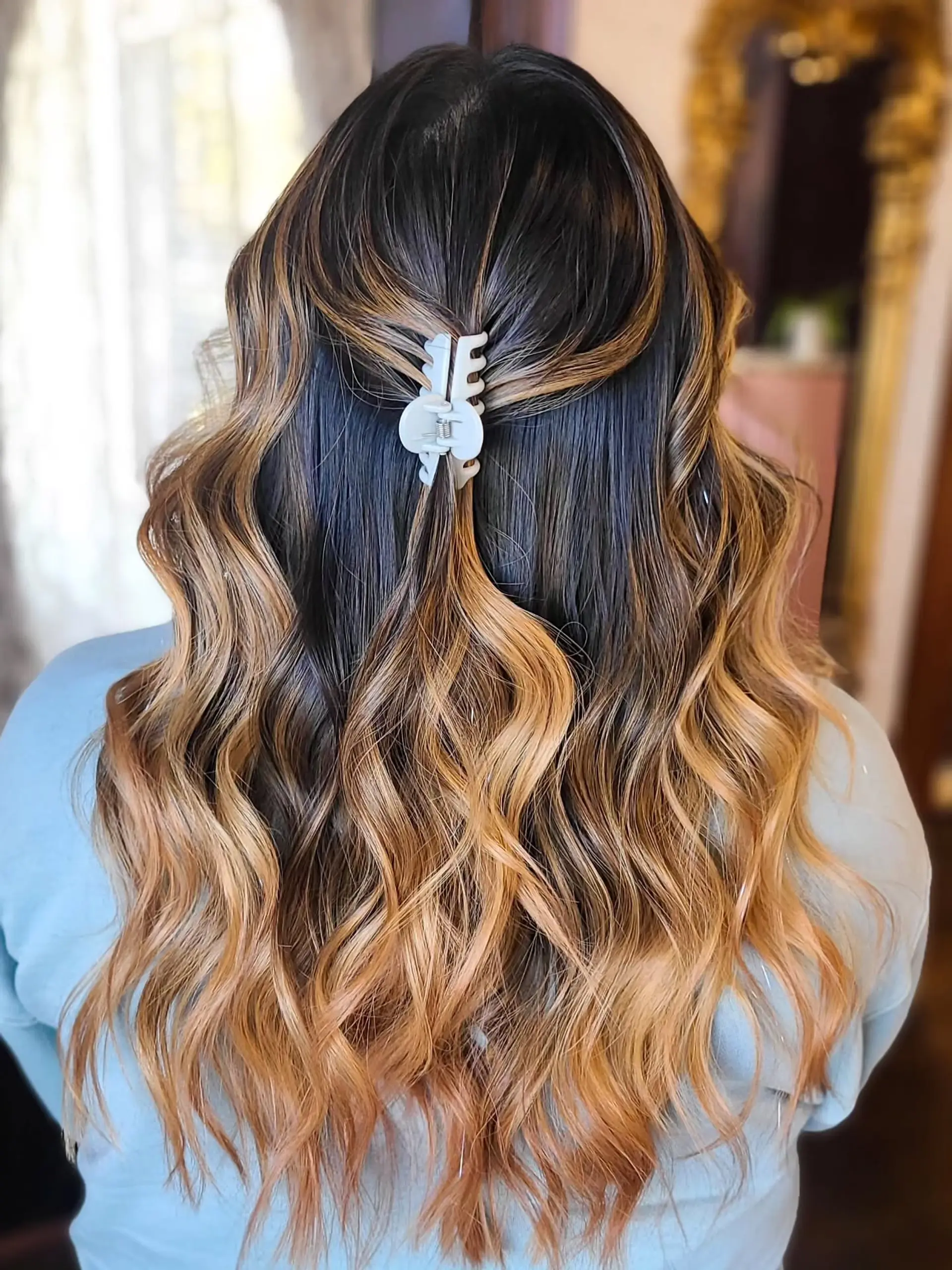 Long, wavy hair with a blended balayage coloring technique that transitions from dark roots to warm caramel and golden blonde ends, styled with soft, loose waves. 1